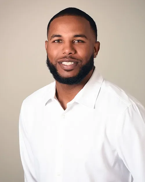 Portrait of a man with a beard and short hair, wearing a white button-up shirt, smiling against a plain background.