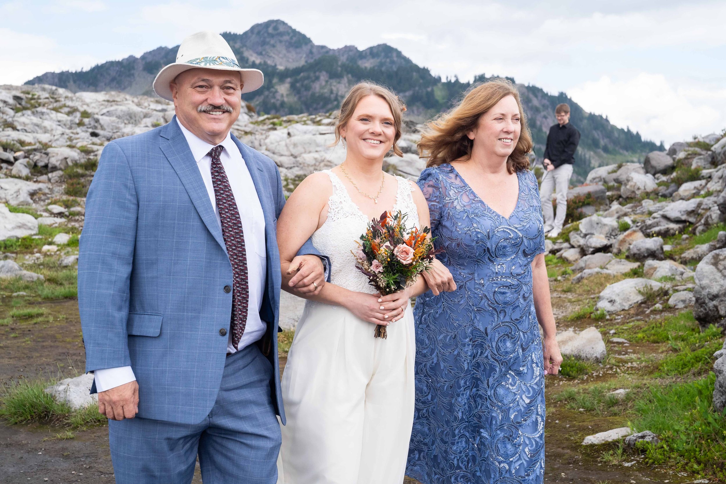 Photo of a bride smiling and walking with her parents towards her wedding ceremony at Artist Point.