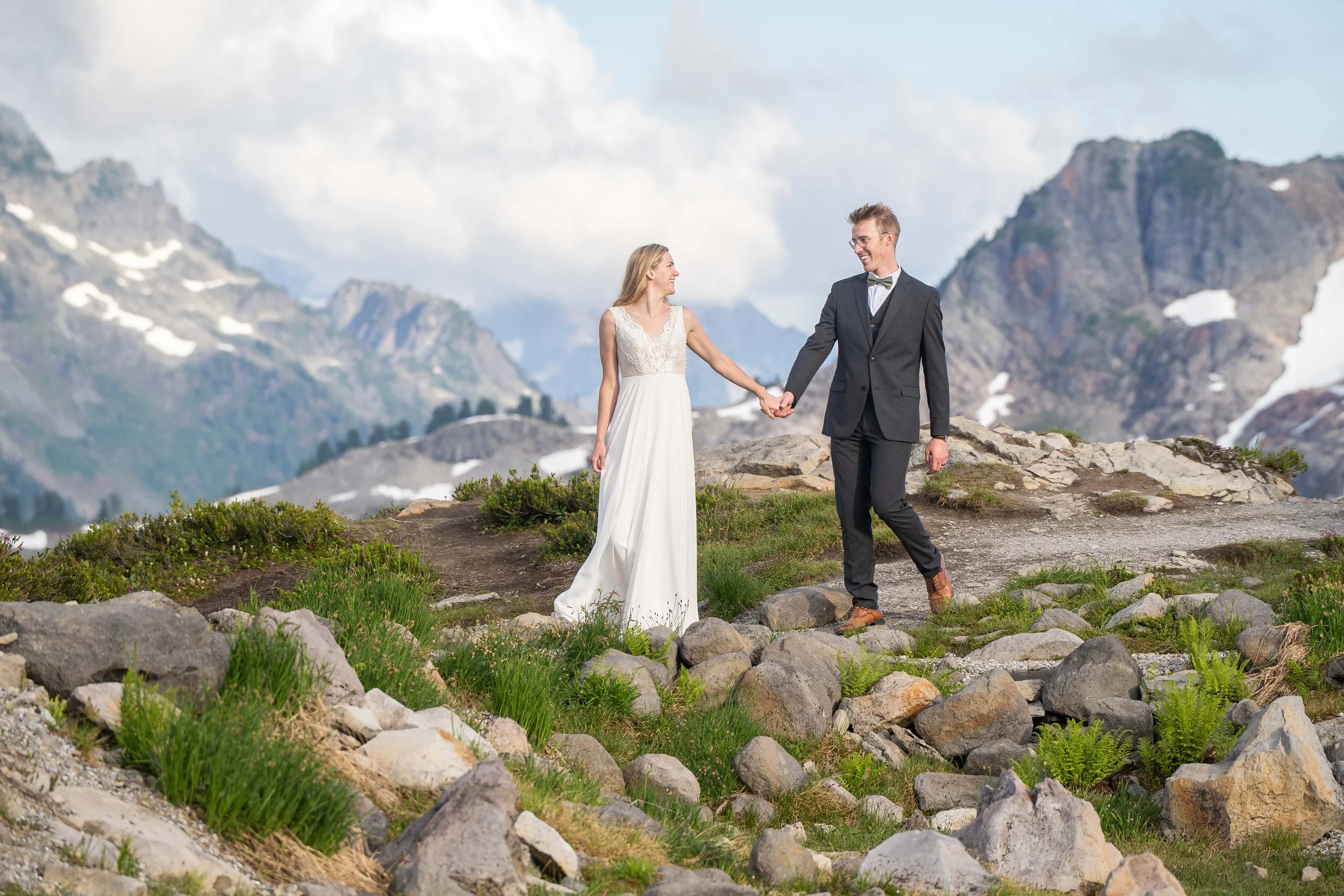 Photo of a couple in a wedding dress and suit eloping at Artist Point at sunset, with alpine meadows in front of them and the North Cascades behind.