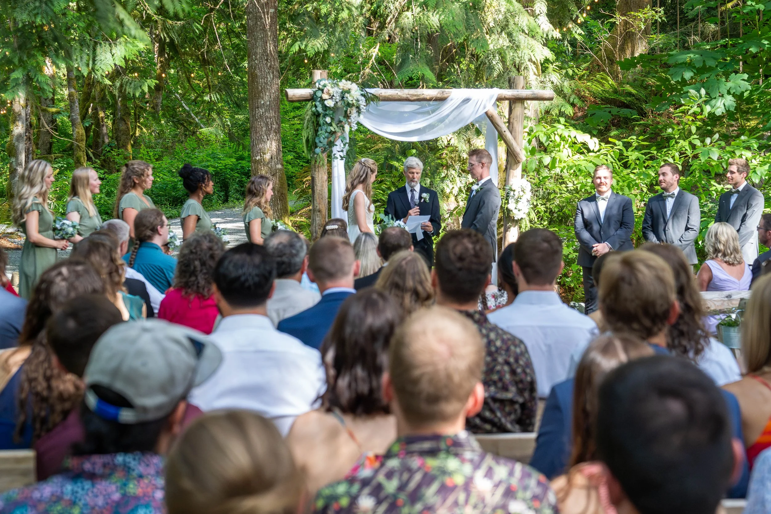 A telephoto image of a couple getting married at an altar in the forest in Skagit County, Washington, with a crowd of wedding guests seated in front of them.