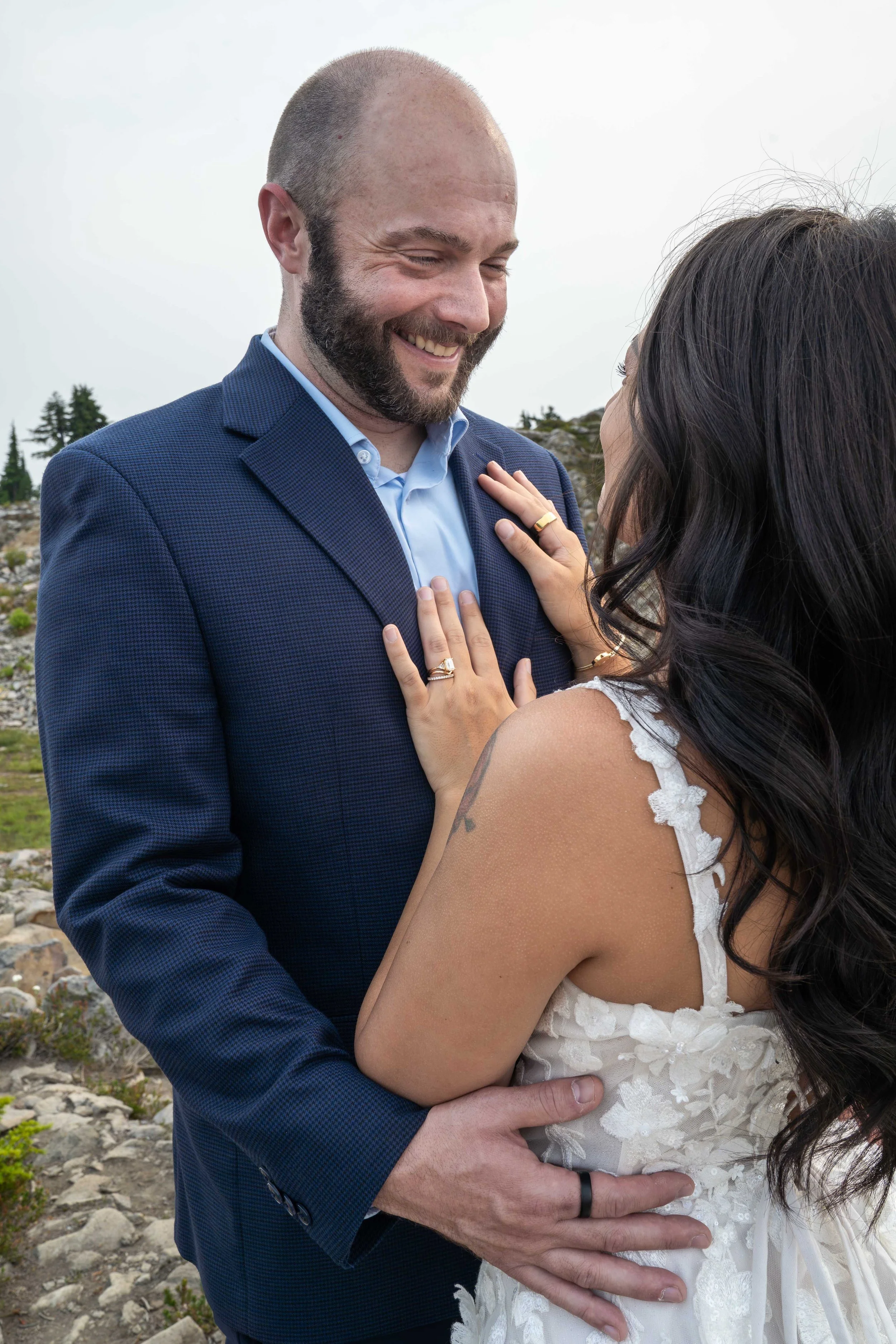 A bride and groom standing together during their Artist Point elopement. The bride has her hands on the groom's chest and her wedding ring is clearly visible.