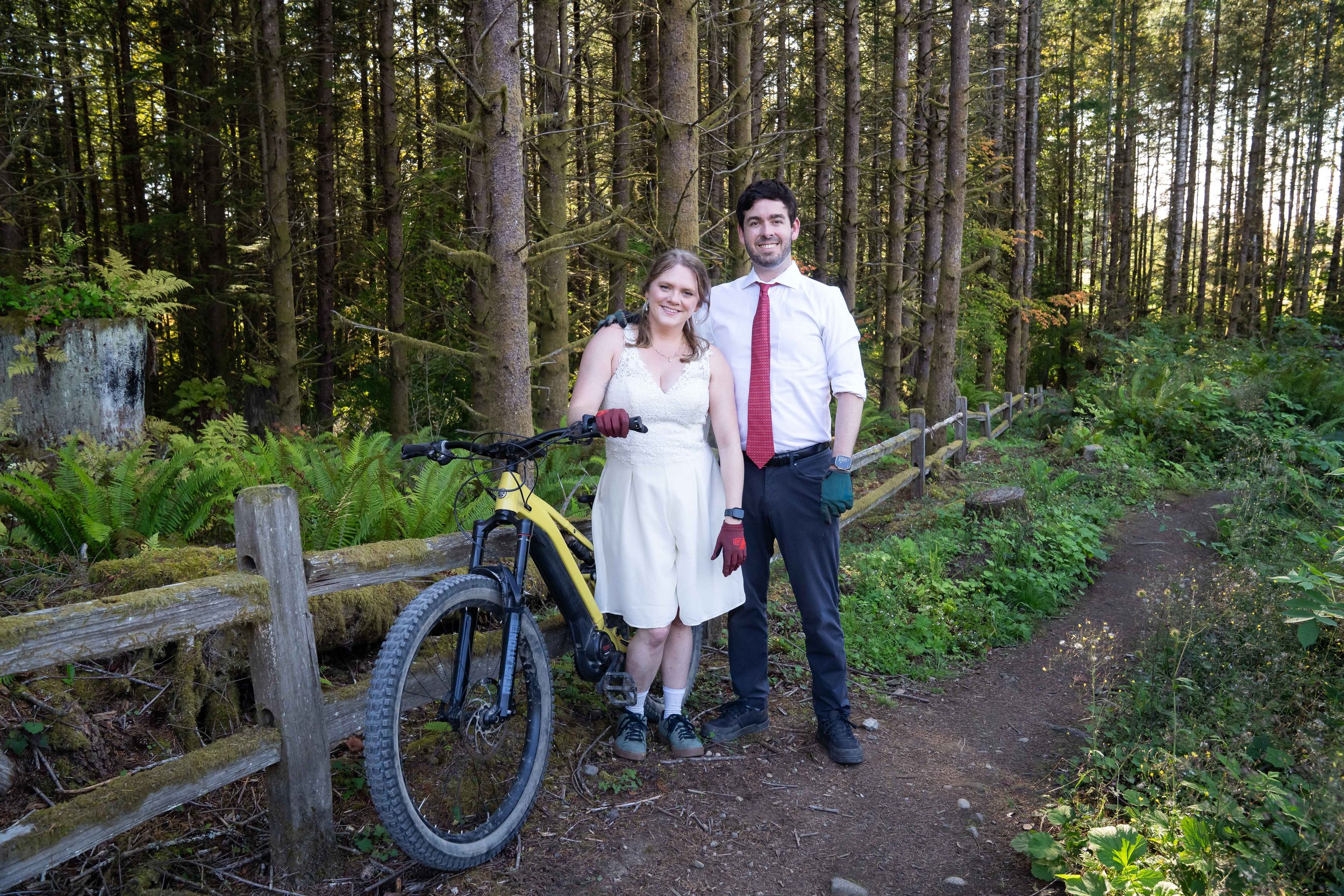 A bride and groom in wedding clothes stand together with a mountain bike during their mountain biking elopement on Galbraith Mountain in Bellingham, Washington