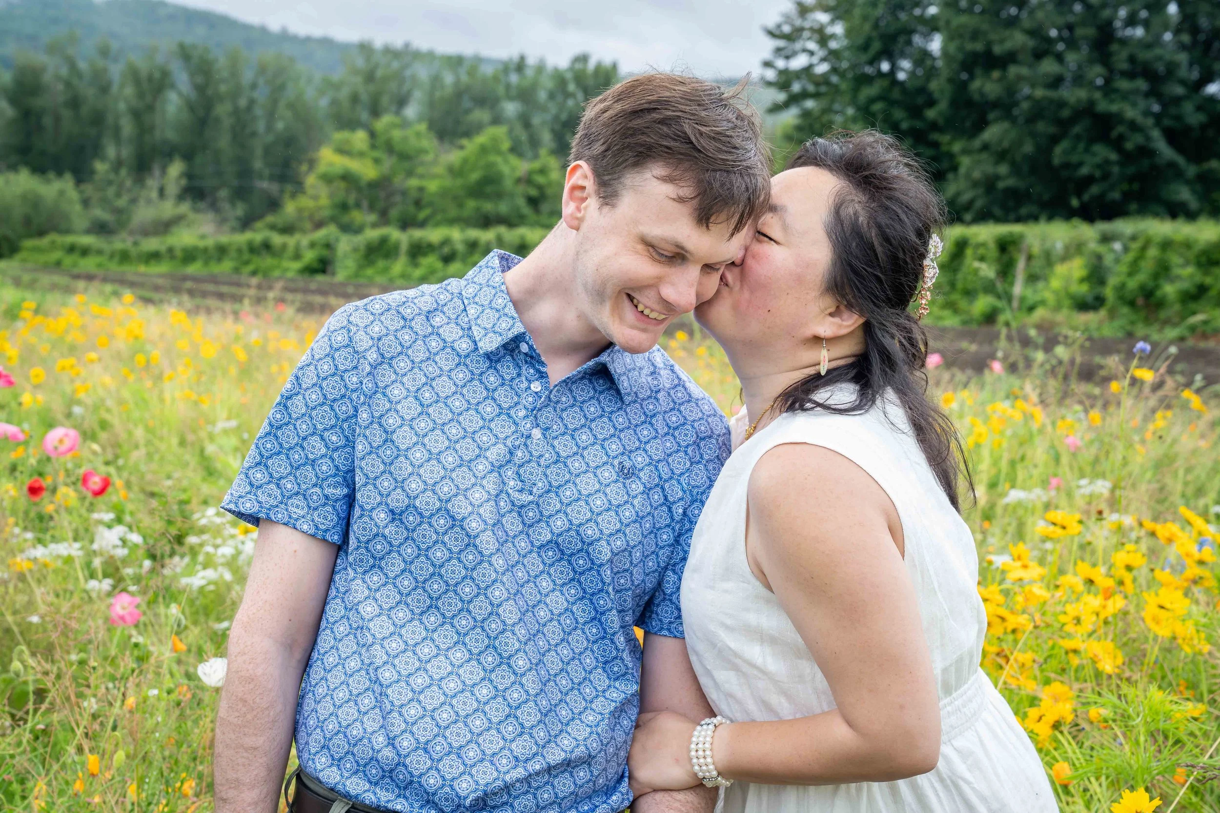 Photo of a couple standing together and the woman kissing the man during a Bellingham elopement photography session. They are standing in a field of flowers.