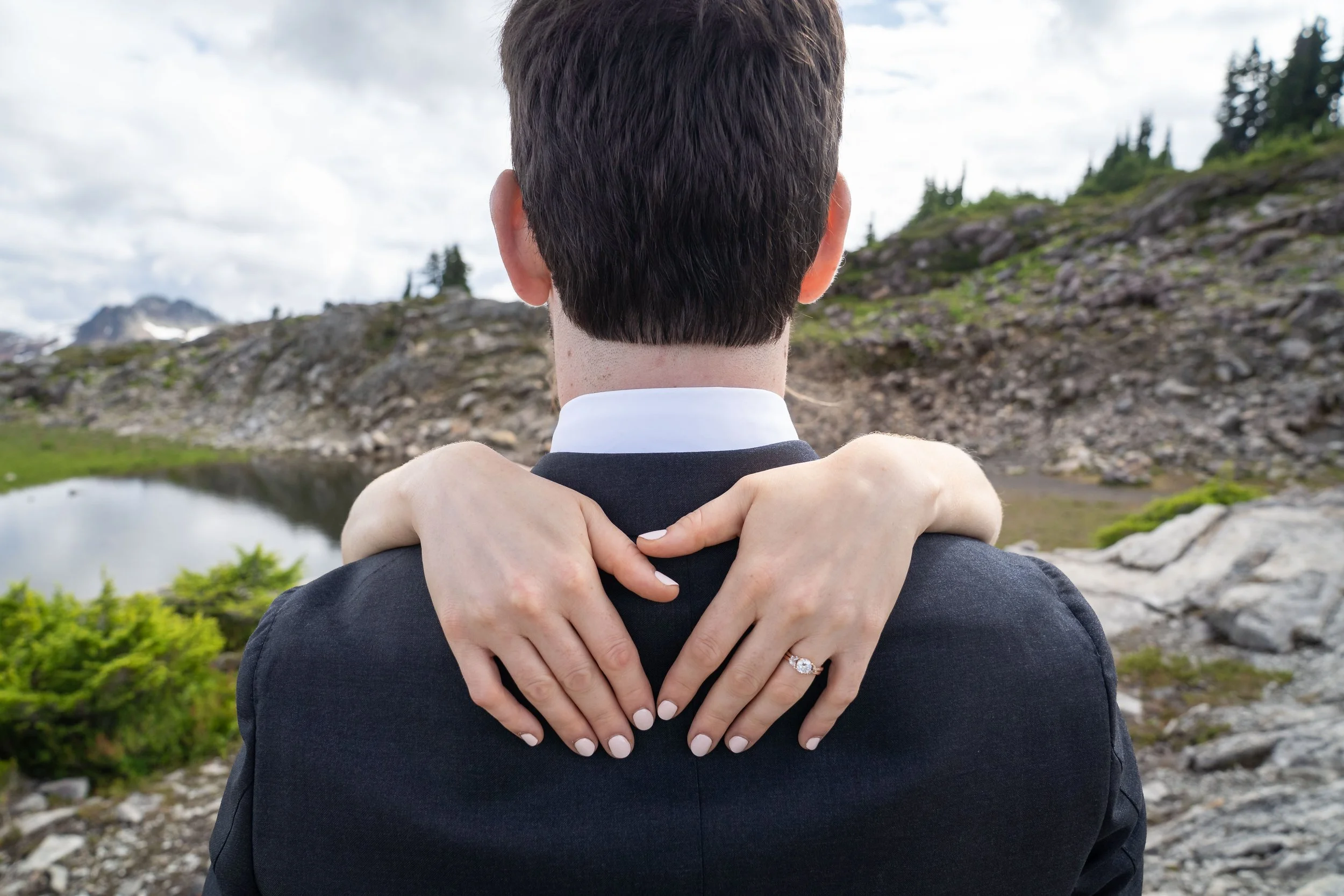 A bride holding her hands over her groom's shoulder so that her wedding ring is clearly visible during an Artist Point hybrid elopement photoshoot.