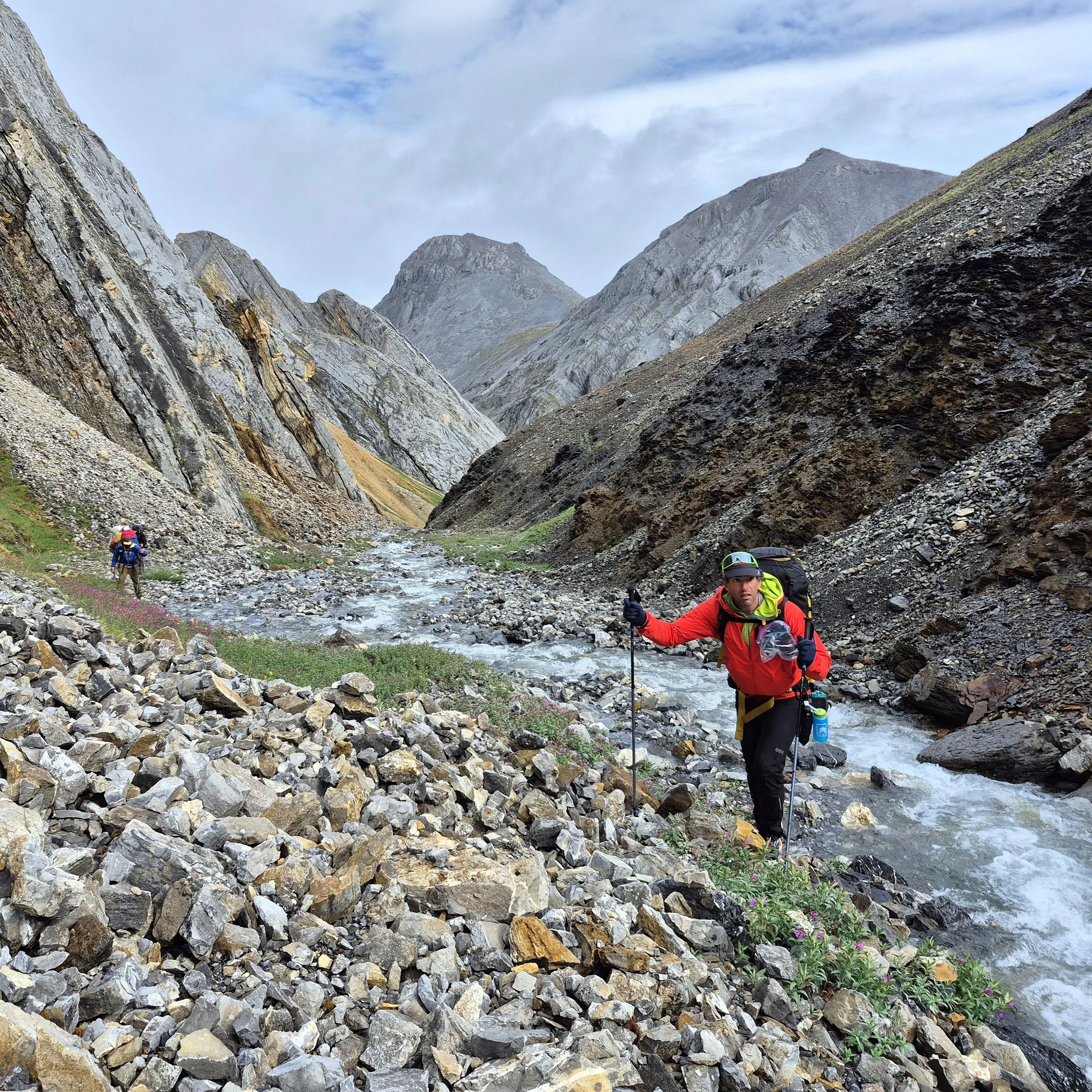 Michael, the photographer behind Wandering Sole Studios, trekking through the Brooks Range of Alaska. He is walking along a rushing river with mountains in the background.