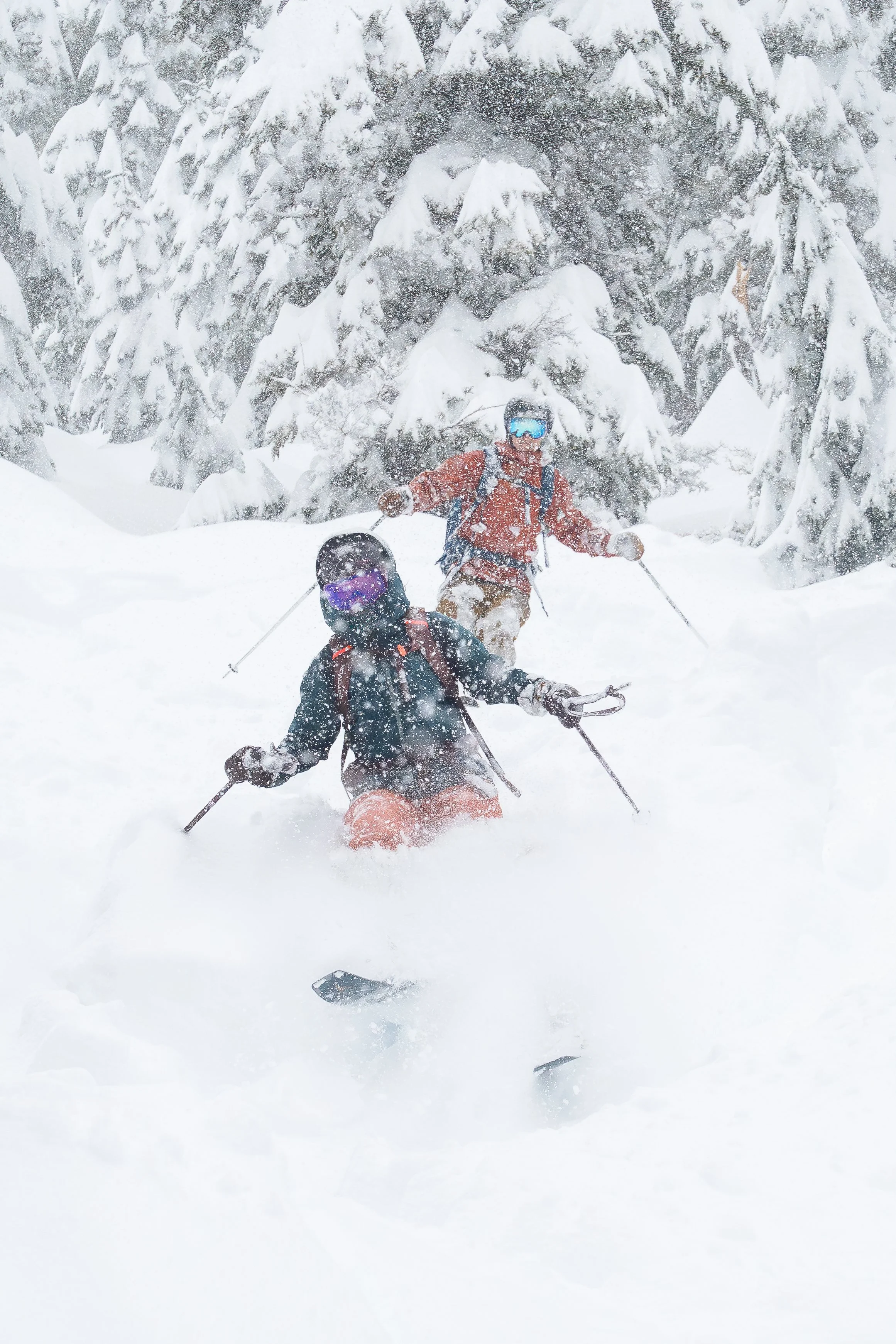 Photo of a couple skiing through deep powder in the backcountry around Snoqualmie Pass, Washington, during a heavy snowstorm. The snow is knee-deep and the woman's skis are creating a cloud of snow.