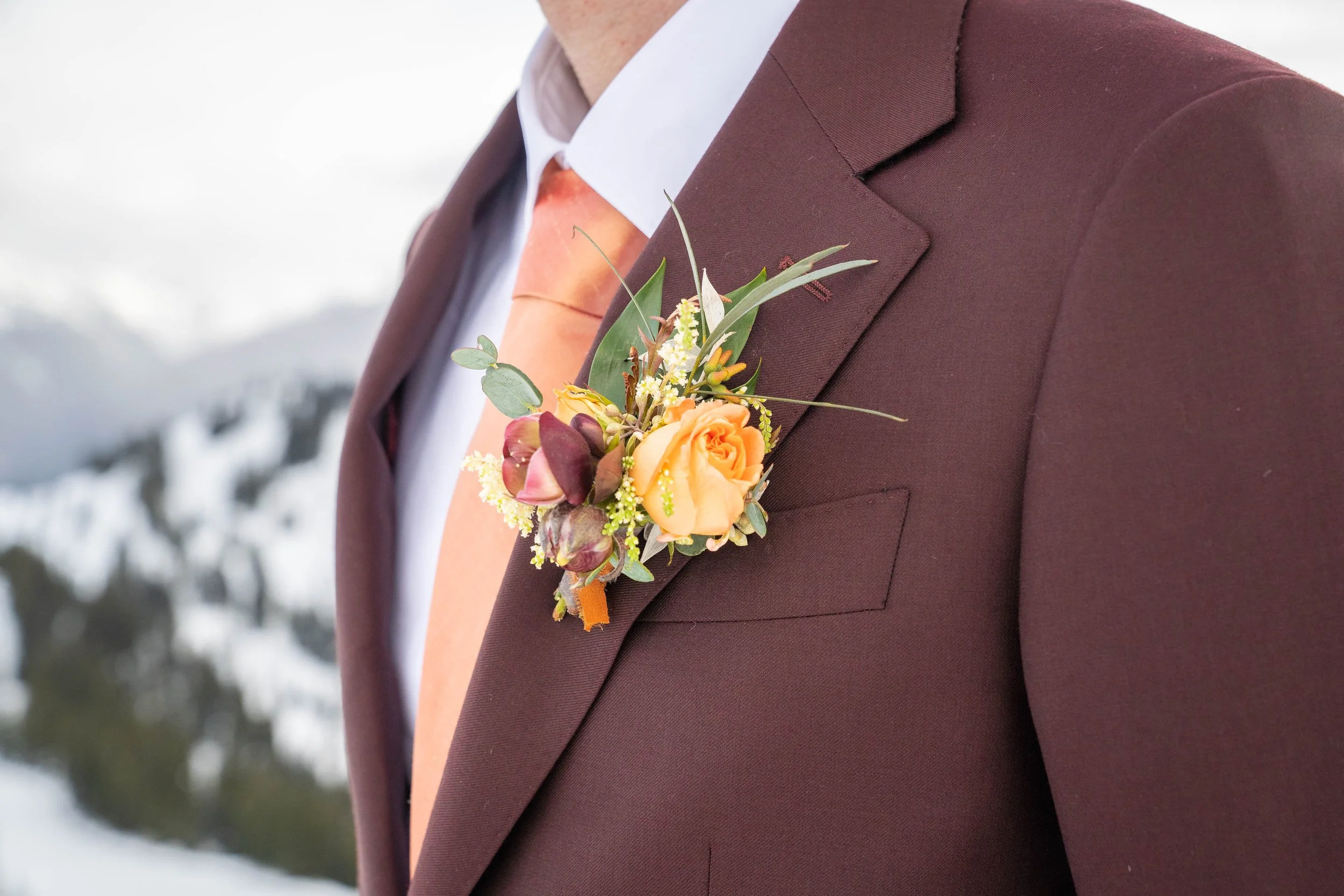 A close-up photo of a groom's brown suit, orange tie, and orange boutonniere.