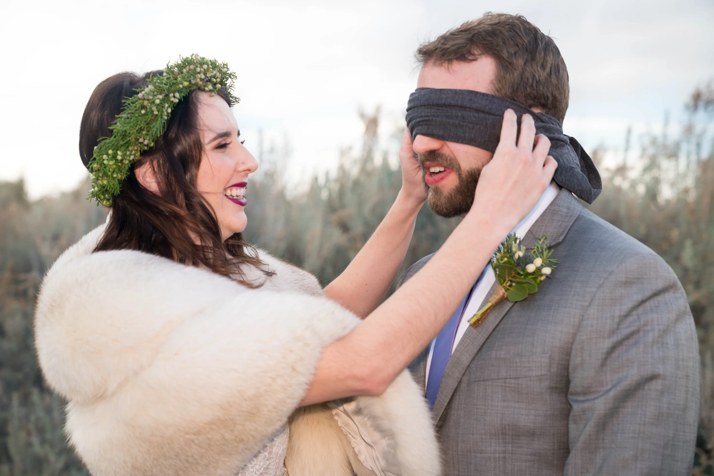 A "first look" photo in which the bride is taking a blindfold off of the groom's eyes.