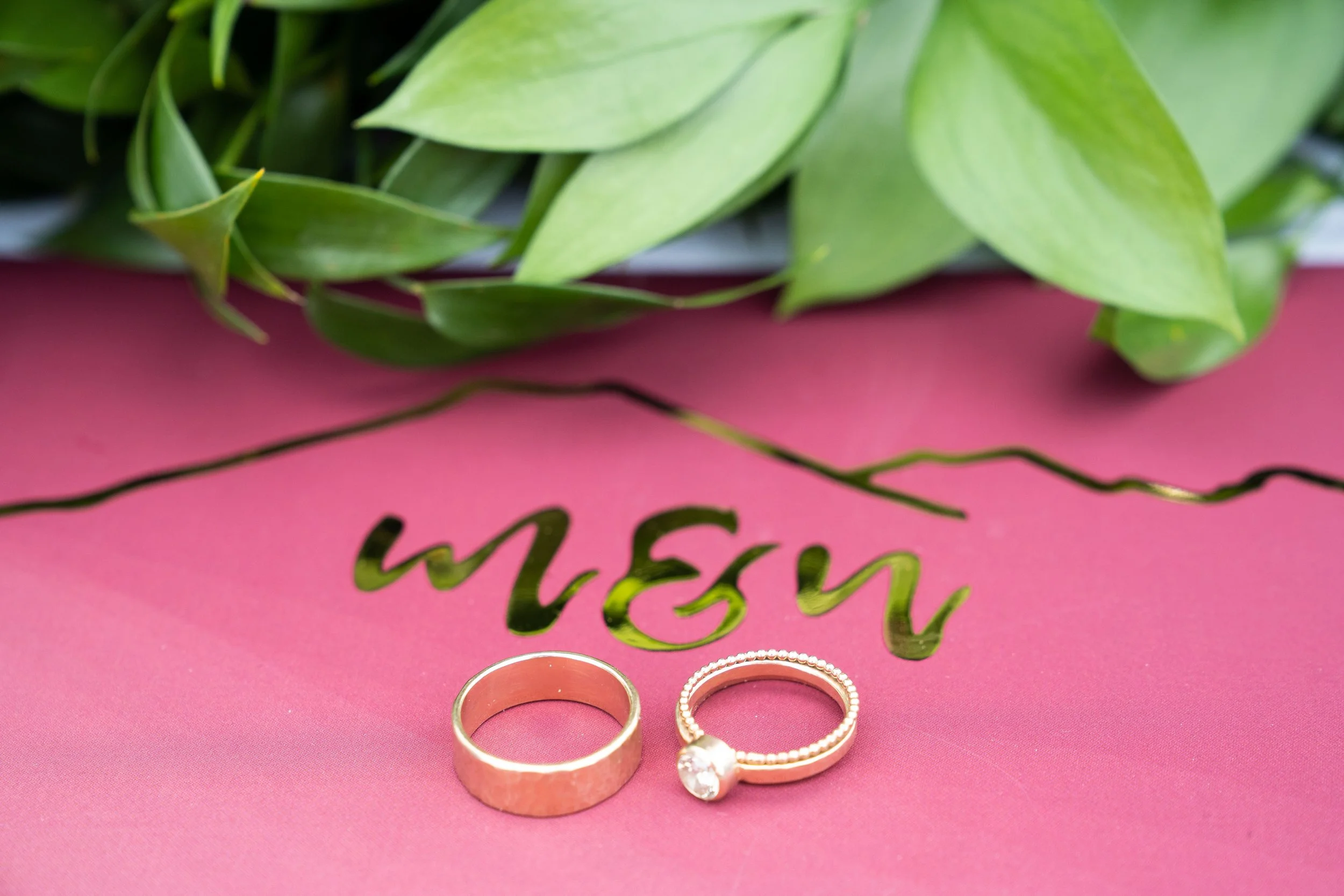 A photo of two wedding rings on a magenta card with the initials M & N stenciled on it.