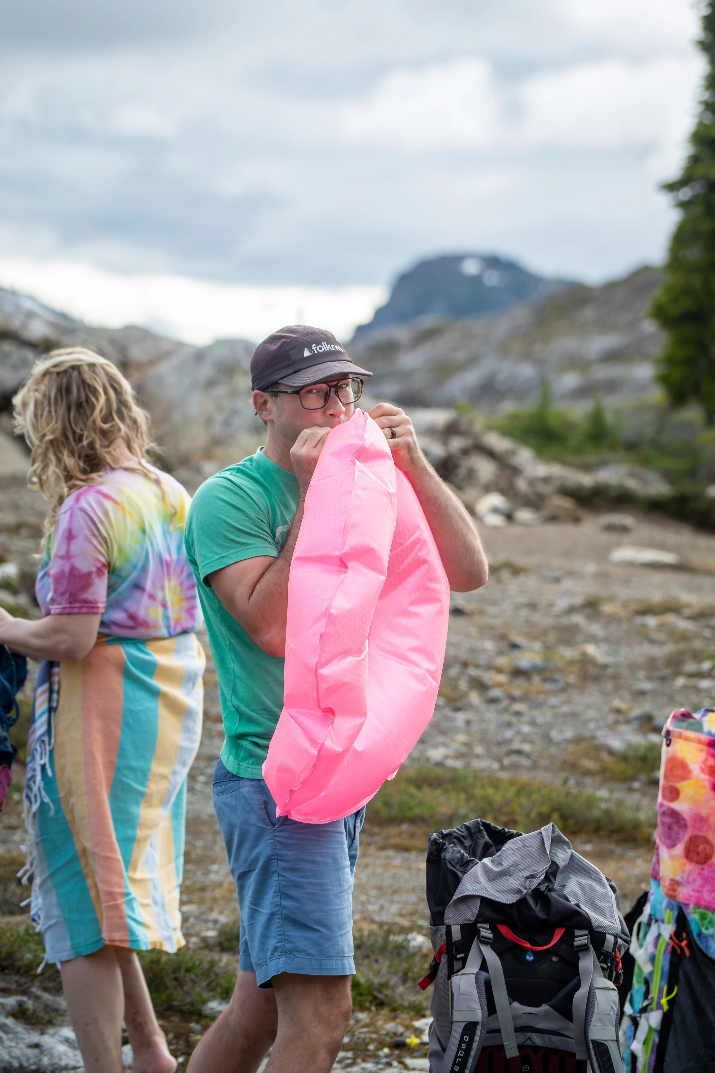 A groom looking at the camera as he inflates a bright pink innertube at the alpine lakes around Yellow Aster Butte and the High Divide trail.