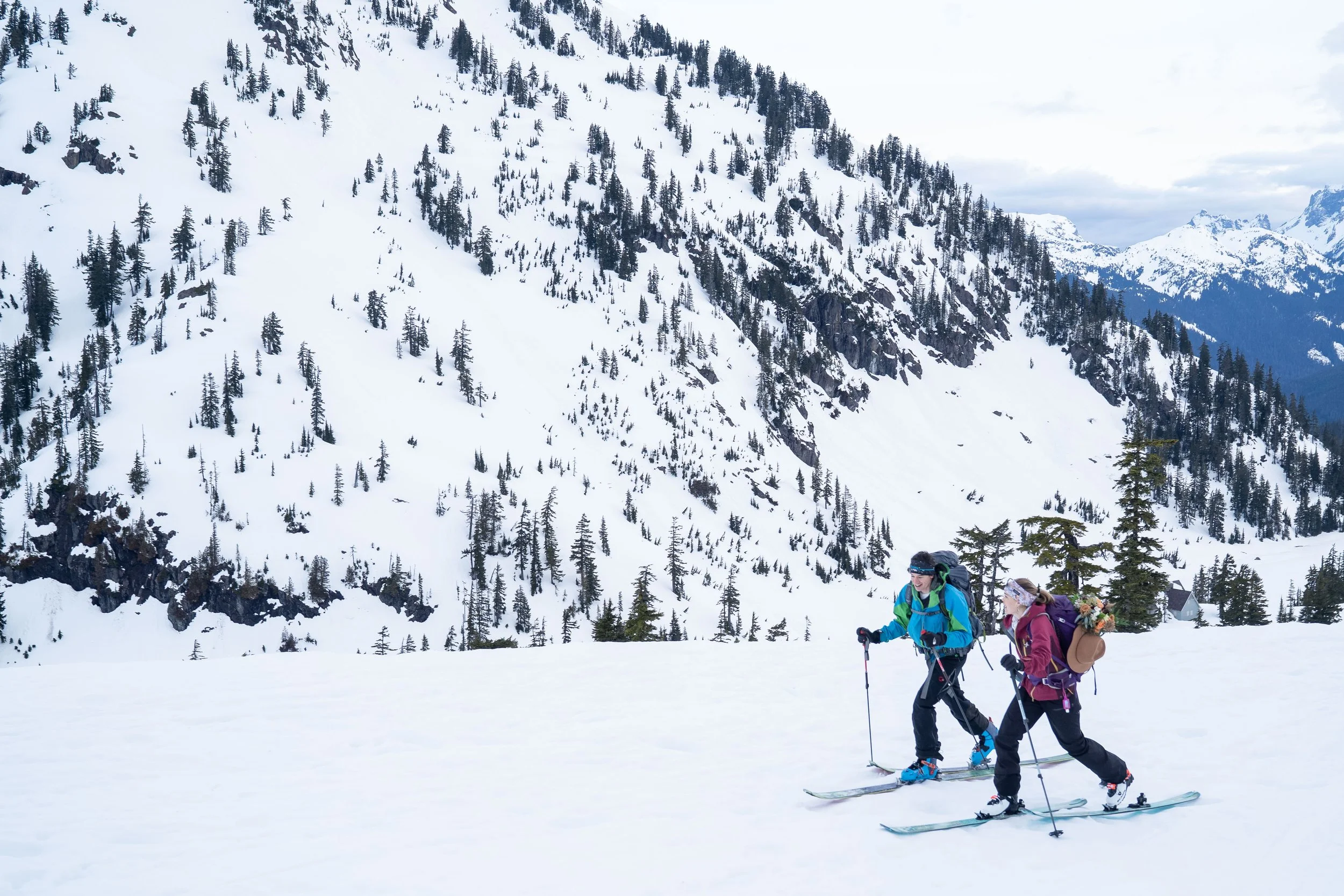 A couple skinning uphill on backcountry skis in the Baker Backcountry, near Artist Point. The woman has a formal hat and flowers attached to her backpack.