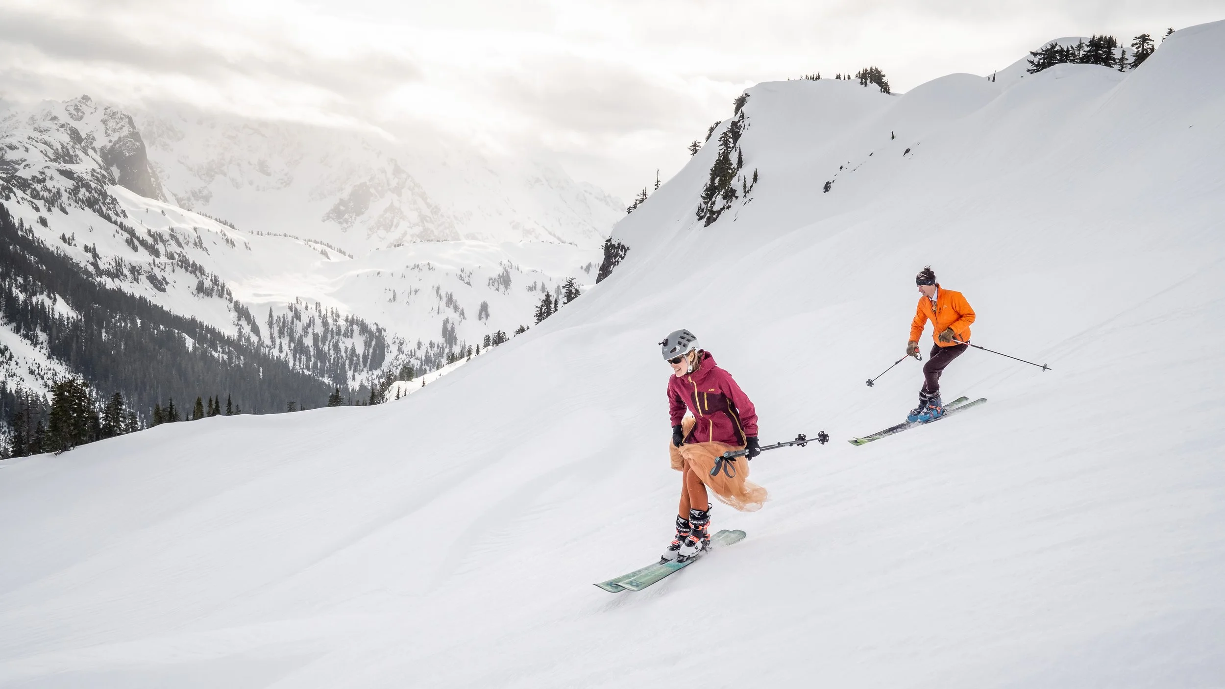 A photo of a bride in a wedding dress and groom in a suit skiing down from Artist Point with Mt. Shuksan in the background during a Mt. Baker ski elopement.
