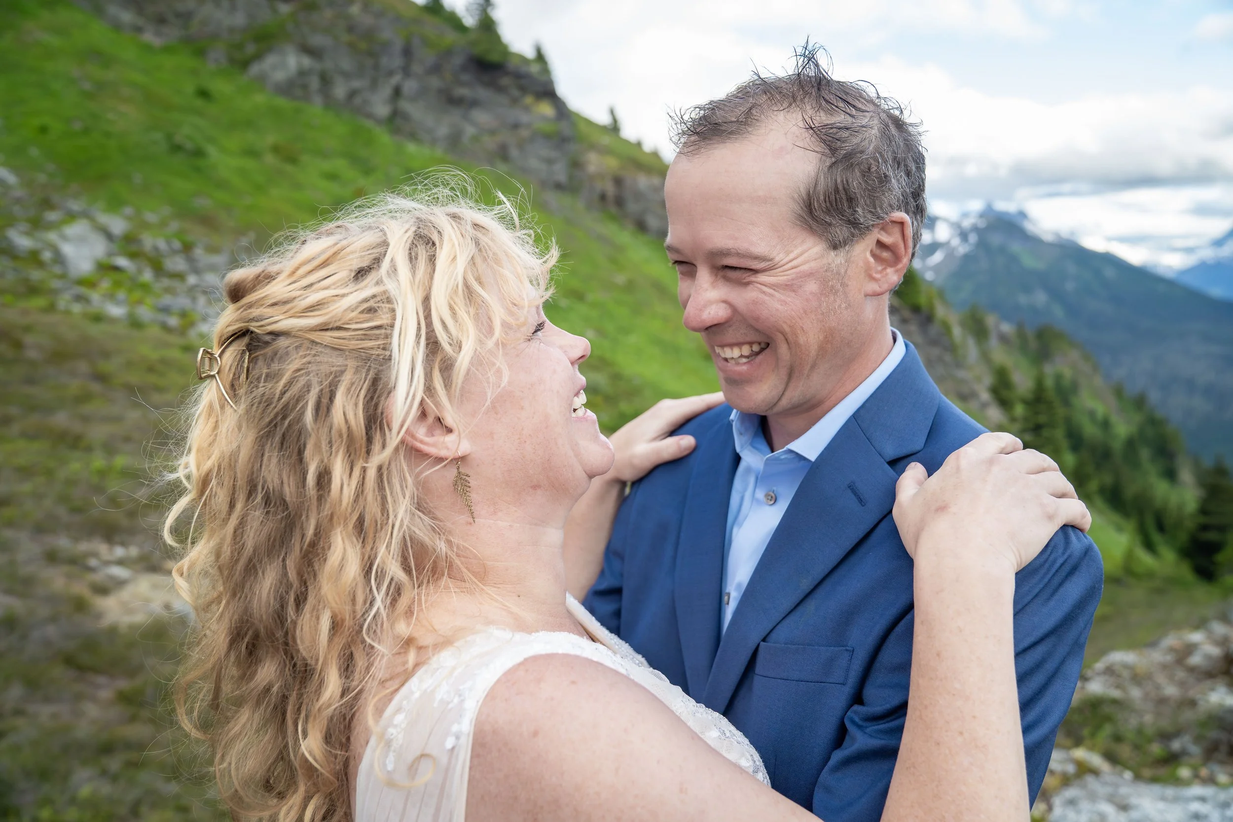 A bride and groom smiling and laughing during their summertime North Cascades elopement at Yellow Aster Butte, with Mt. Shuksan visible behind them.