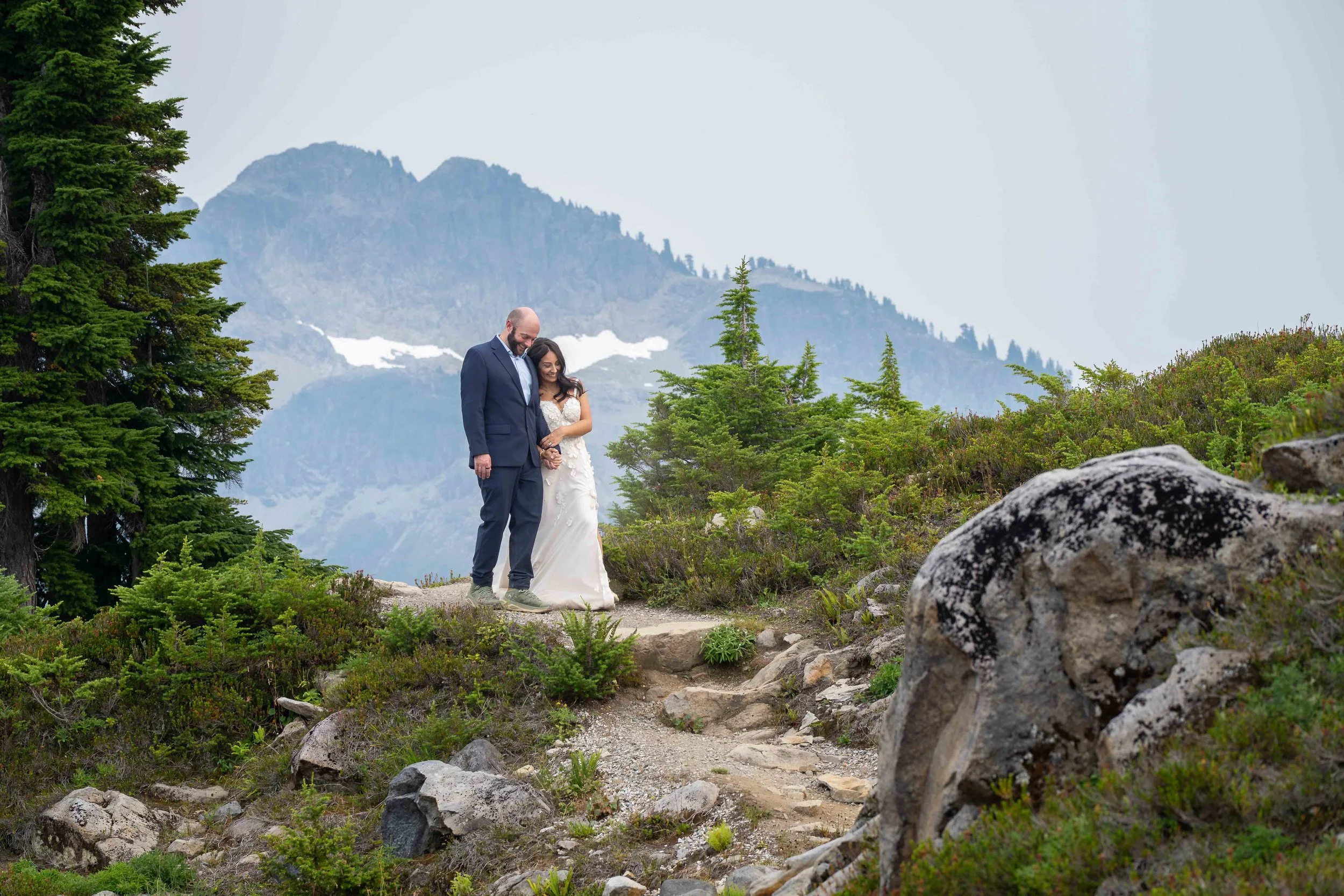 A bride and groom in wedding clothes walk together through a subalpine meadow at Artist Point during their Mt. Baker elopement. Mt. Shuksan is visible in the background.