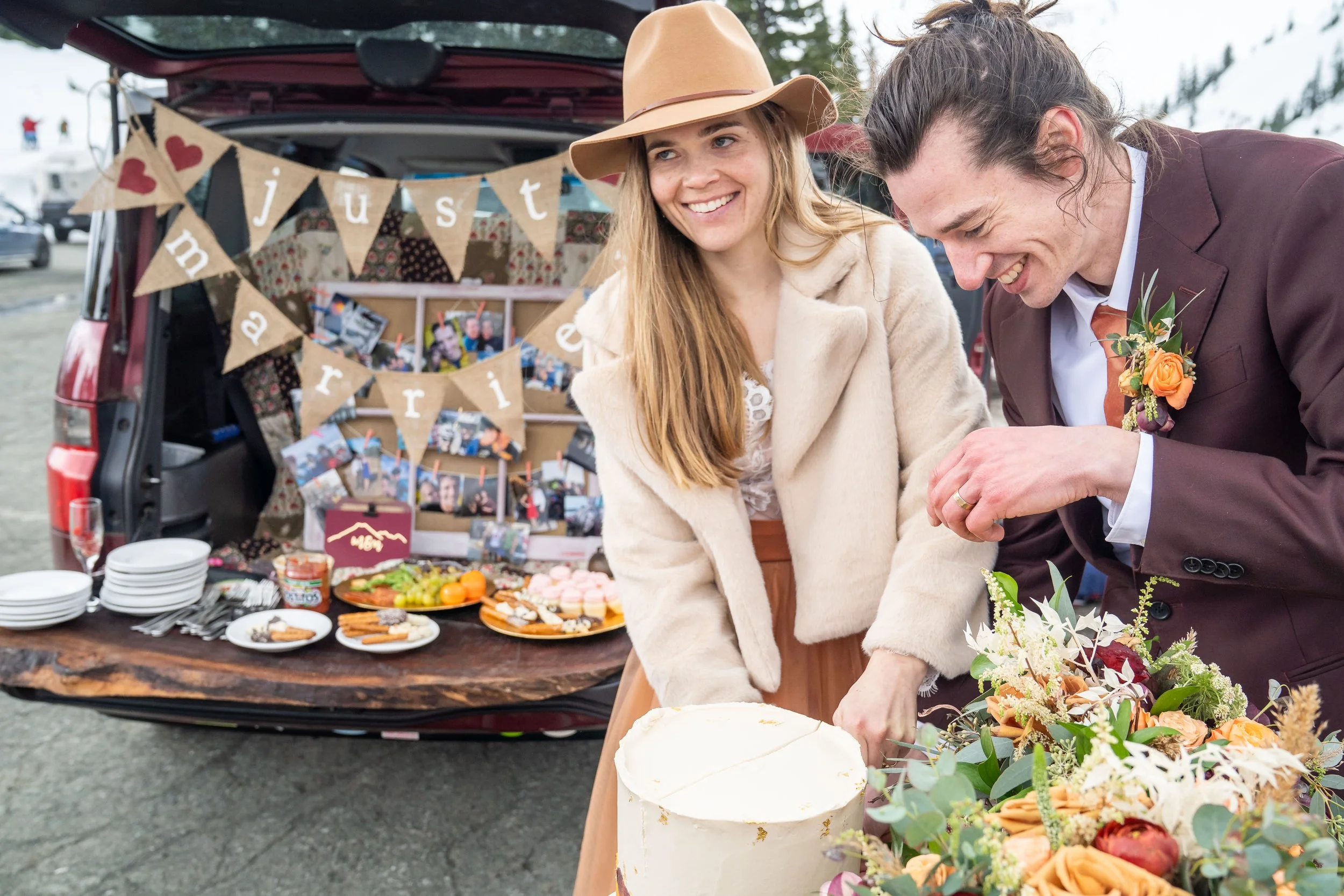 A photo of a bride and groom cutting their wedding cake together. There are flowers in the foreground and a sign that says Just Married in the background.