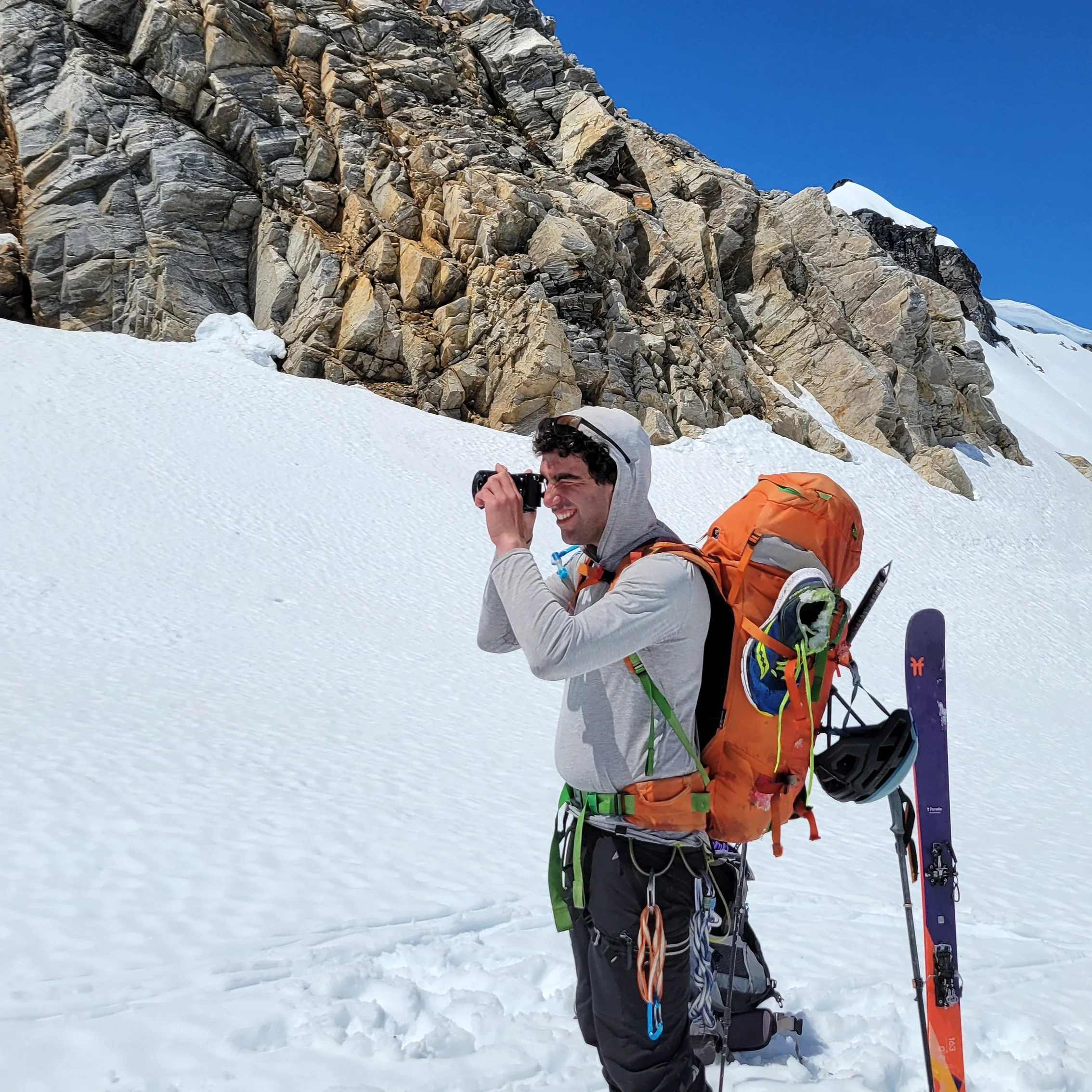 Michael, the photographer behind Wandering Sole Studios, taking photos while wearing a full backpack and climbing harness. He is in the middle of the Ptarmigan Traverse on a snow-covered glacier.