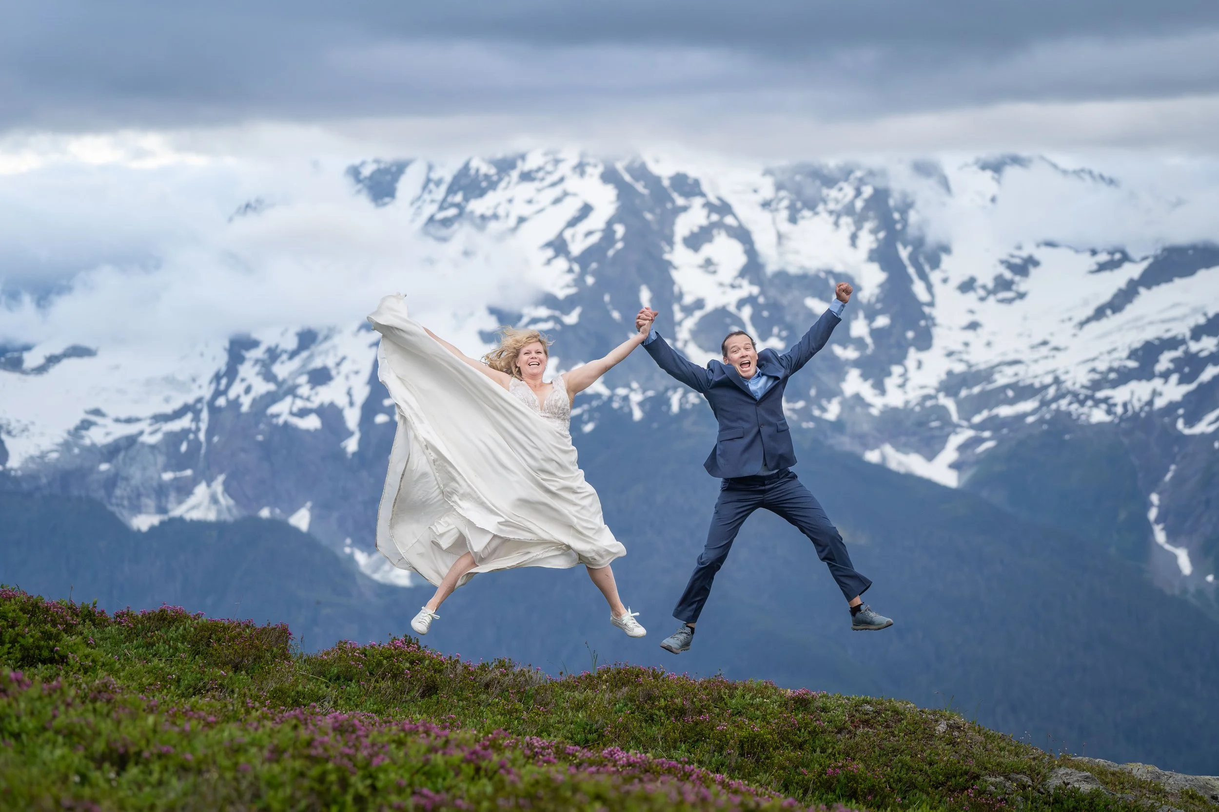 A bride and groom jump into the air holding hands with Mount Shuksan behind them during their Yellow Aster Butte elopement.