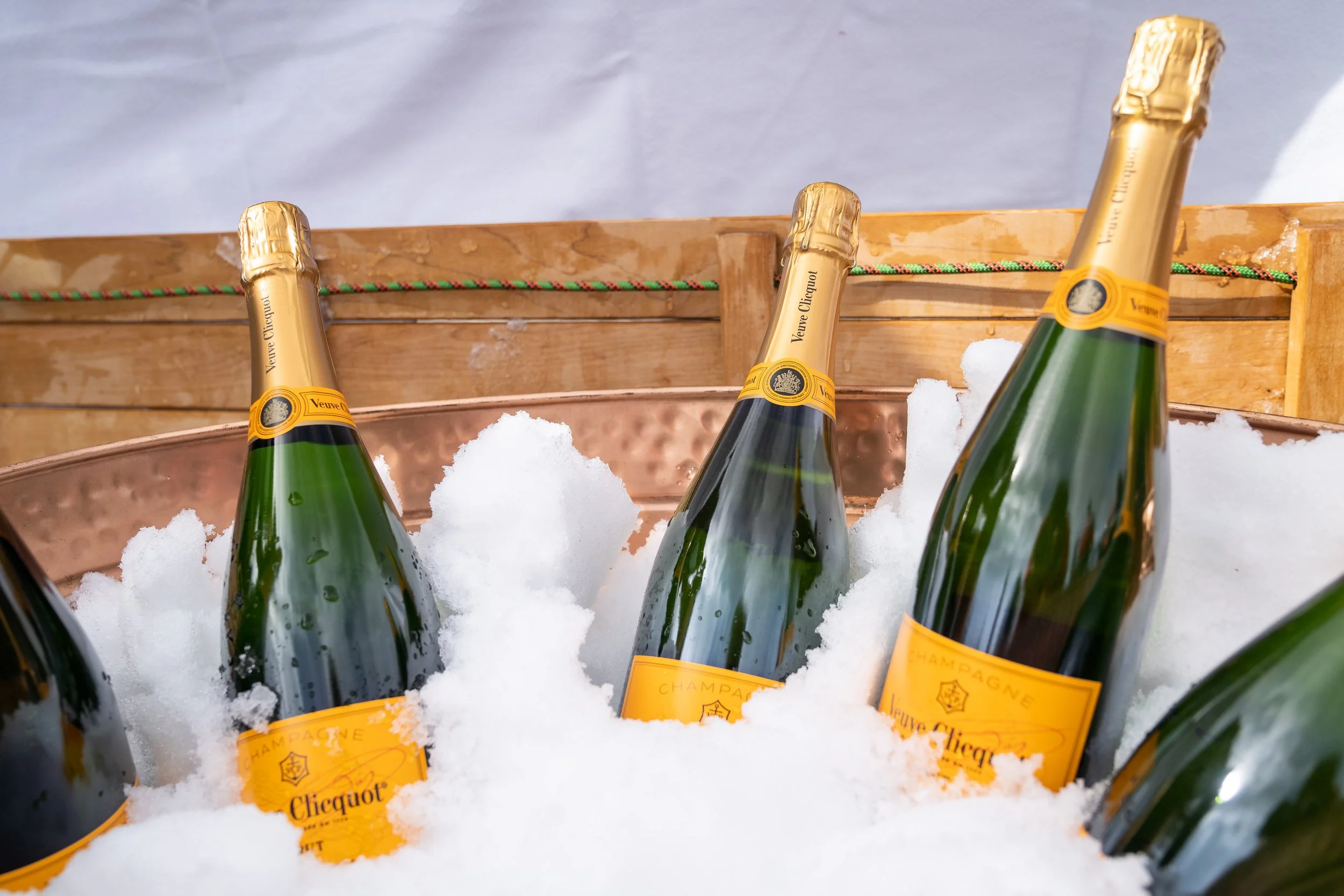 A photo of several bottles of champagne sitting in a wooden ice bucket filled with snow.