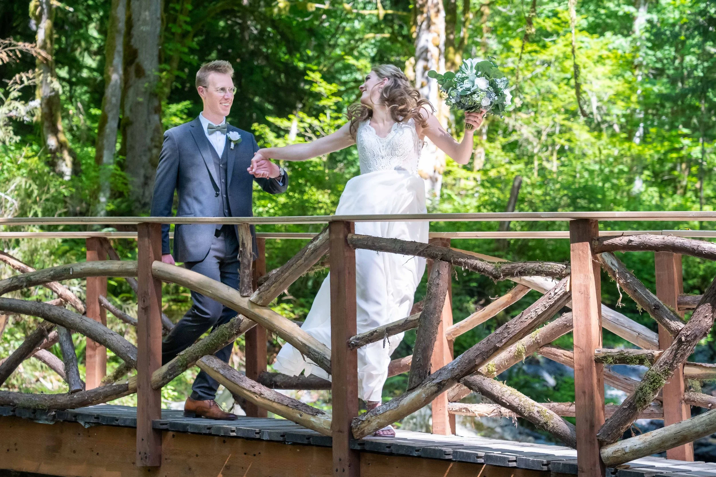 A photo of a bride and groom at their wedding holding hands and skipping on a wooden bridge in the forest at Creekside Celebrations in Skagit County, Washington.