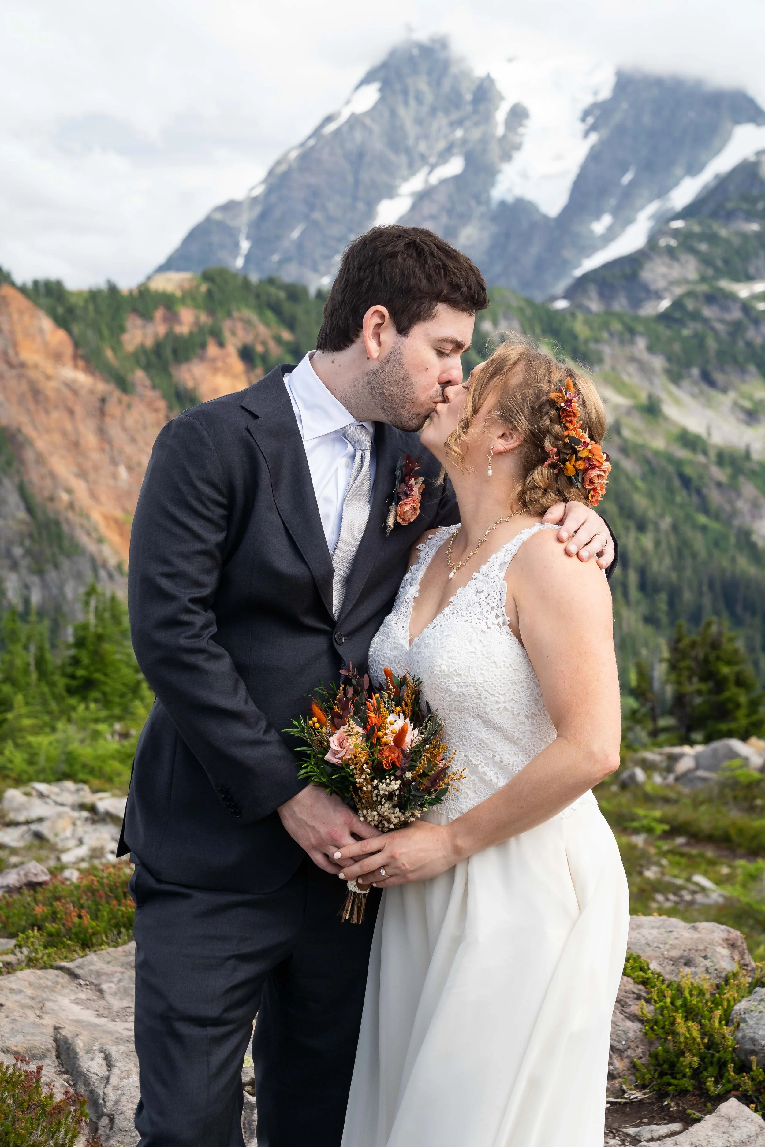 Photo of a bride and groom kissing during their Artist Point elopement. The bride and groom are standing together with their hands overlapping on a bouquet and Mount Shuksan is visible behind them.