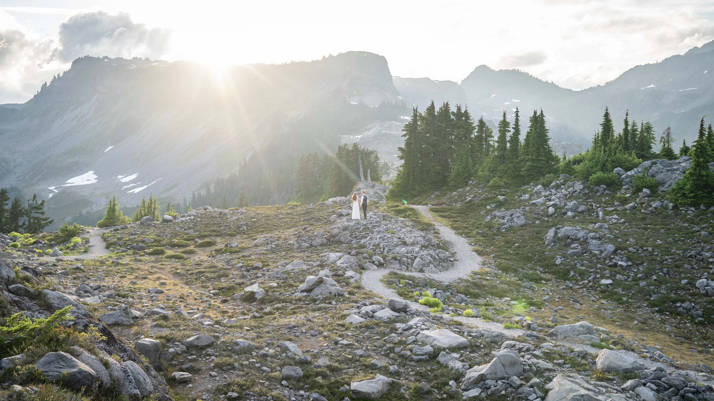 A bride and groom standing together in an alpine meadow after eloping at Artist Point at sunset. They are looking towards Table Mountain as the sun sets over the North Cascades.