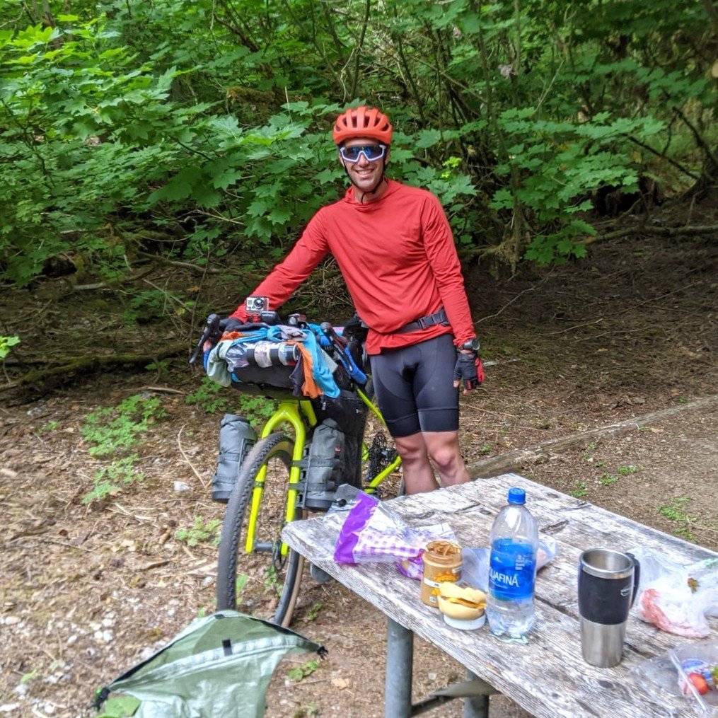 Michael, the photographer behind Wandering Sole Studios, standing at a campground in North Cascades National Park with his bike, which is loaded with multiple bikepacking bags.