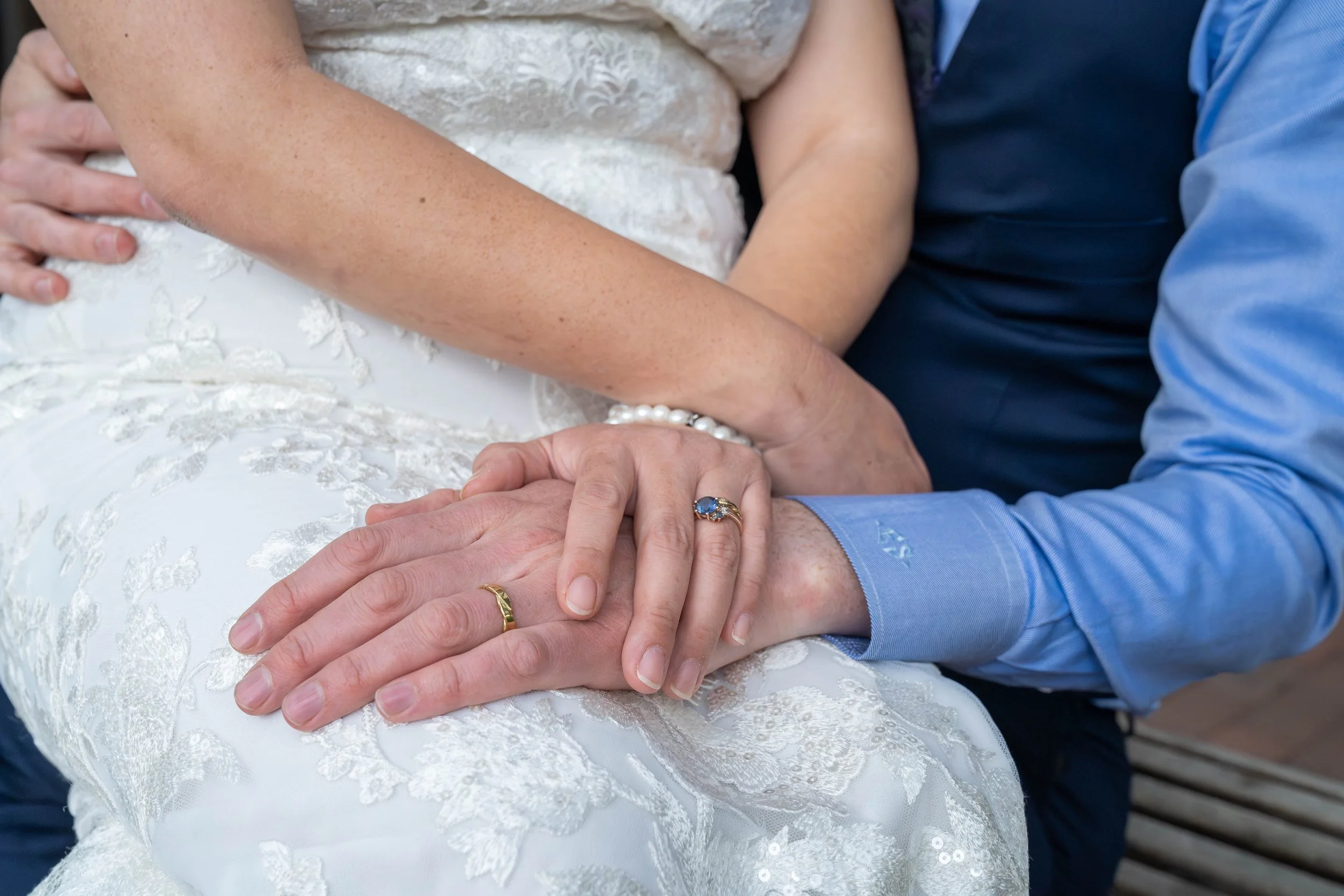 A bride and groom sitting together and holding hands with their wedding rings visible during a Fairhaven elopement in Bellingham, Washington.