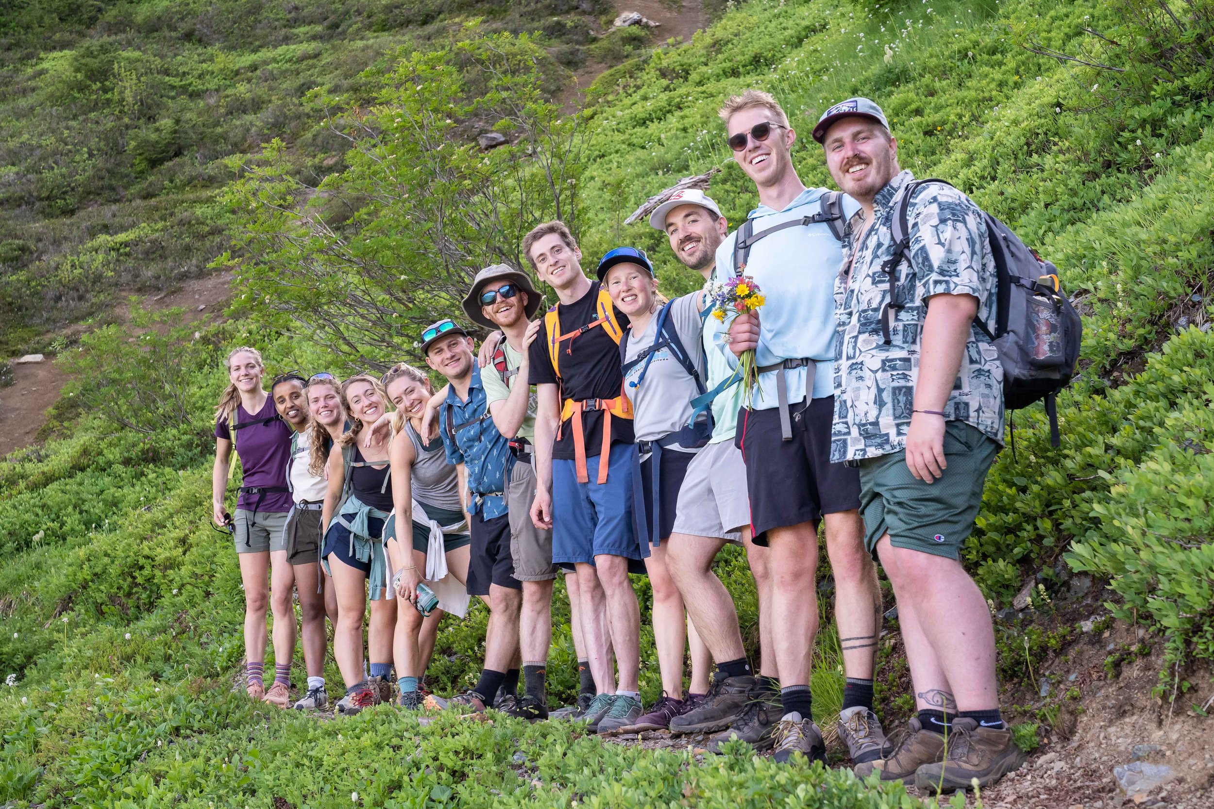 A bridal party in hiking clothes and hiking boots on their way to an elopement in the North Cascades. They are standing together on the trail for a group photo.