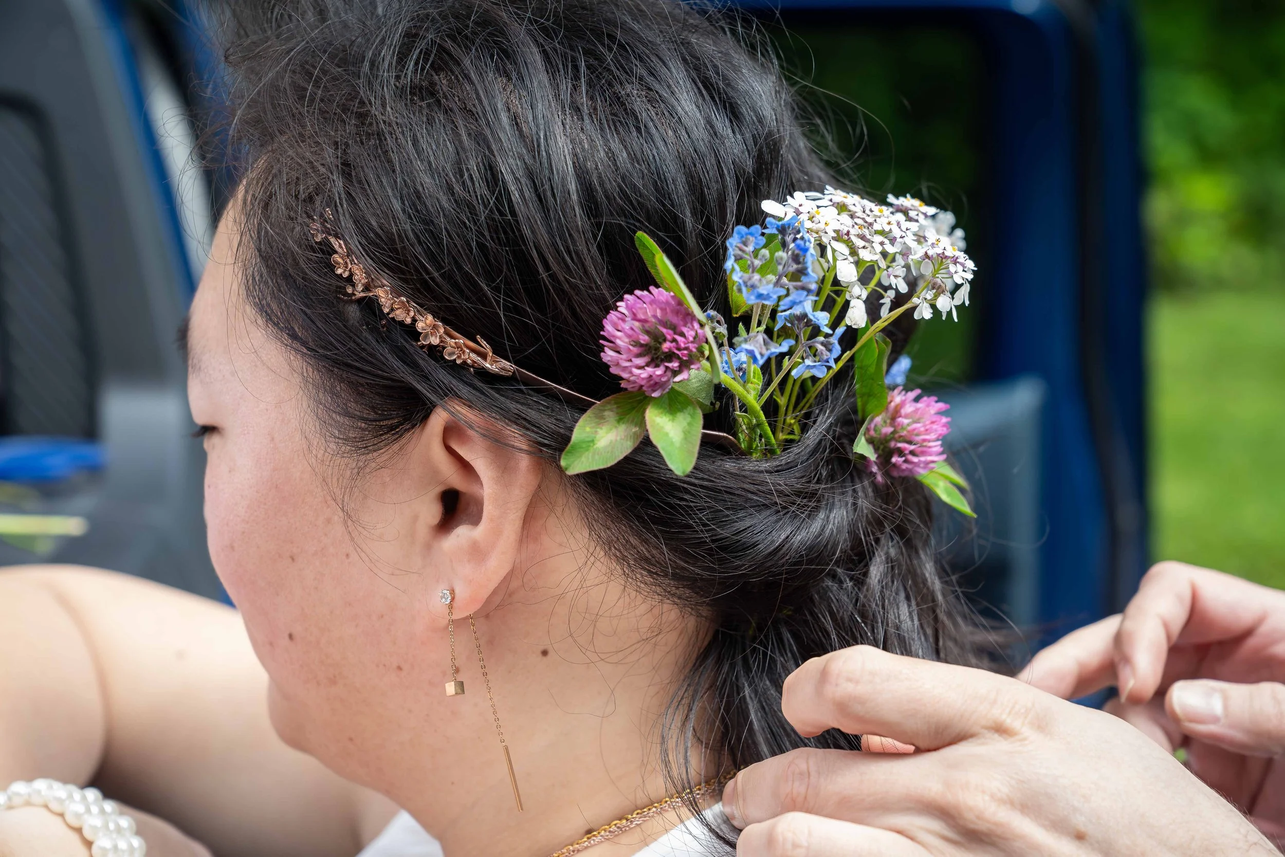 A photo of a bride's hair showing her tiara and flowers knotted into her hair. Her hairdresser's hands are visible in the photo as she prepares for a first look in Larrabee State Park outside Bellingham.
