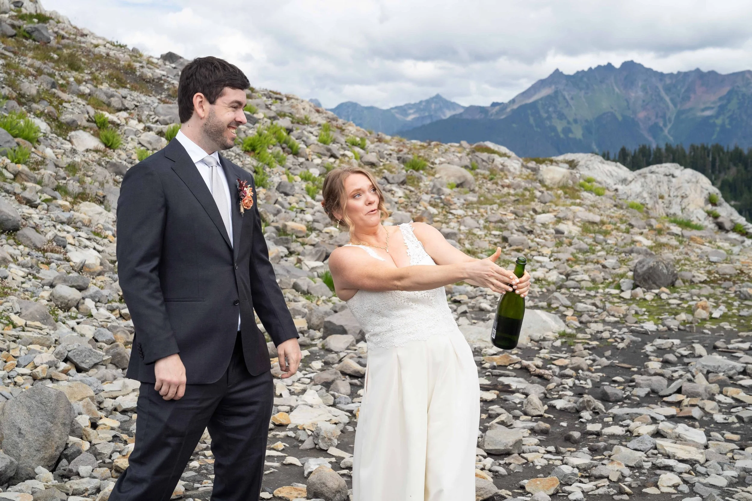 A photo of a bride and groom standing in a rocky alpine basin at Artist Point and celebrating their new marriage by popping champagne. The bride looks concerned as the cork flies out.