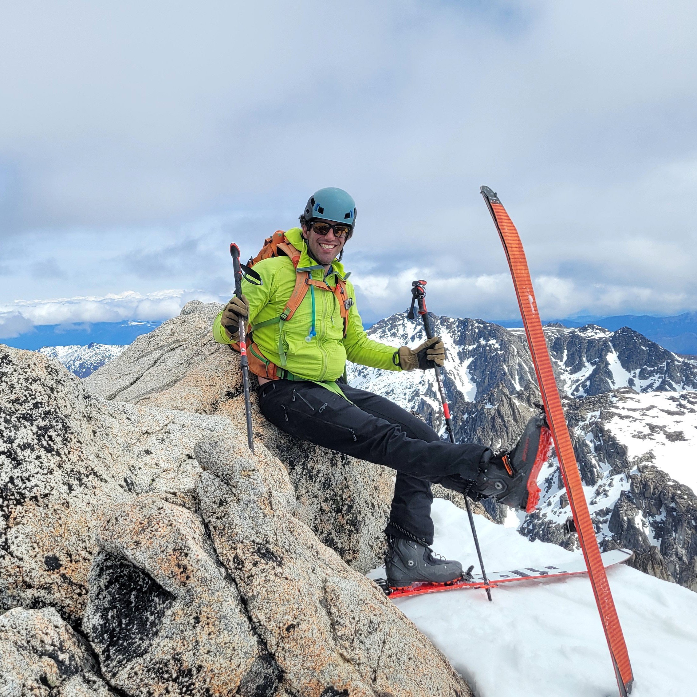 Michael, the photographer behind Wandering Sole Studios, sitting on the snow-covered summit of Dragontail Peak in the Enchantments with his skis on, getting ready to backcountry ski back to Colchuck Lake.