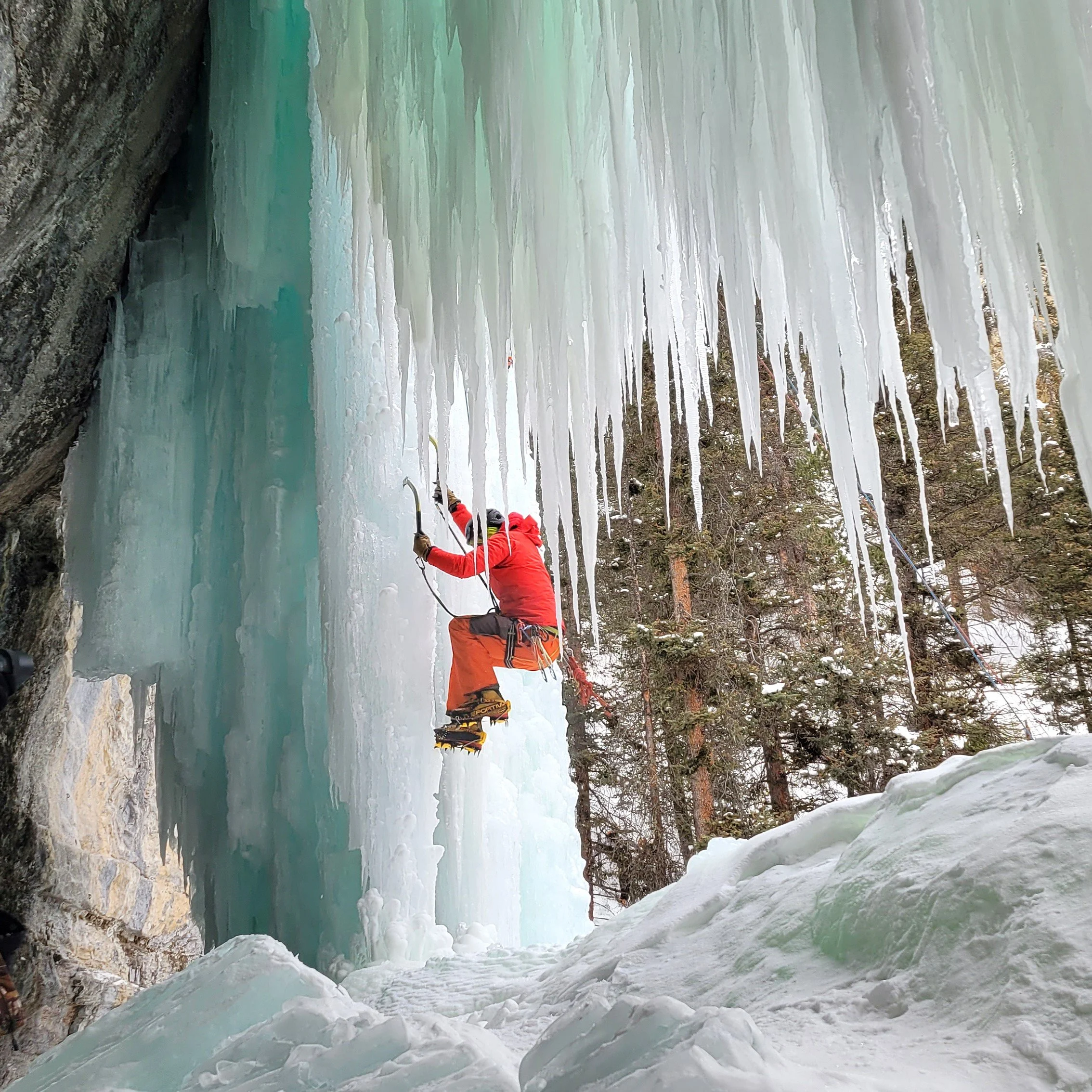 Michael, the photographer behind Wandering Sole Studios, ice climbing a frozen waterfall in Canmore, Alberta. The photo is taken from inside a cave with icicles hanging down.