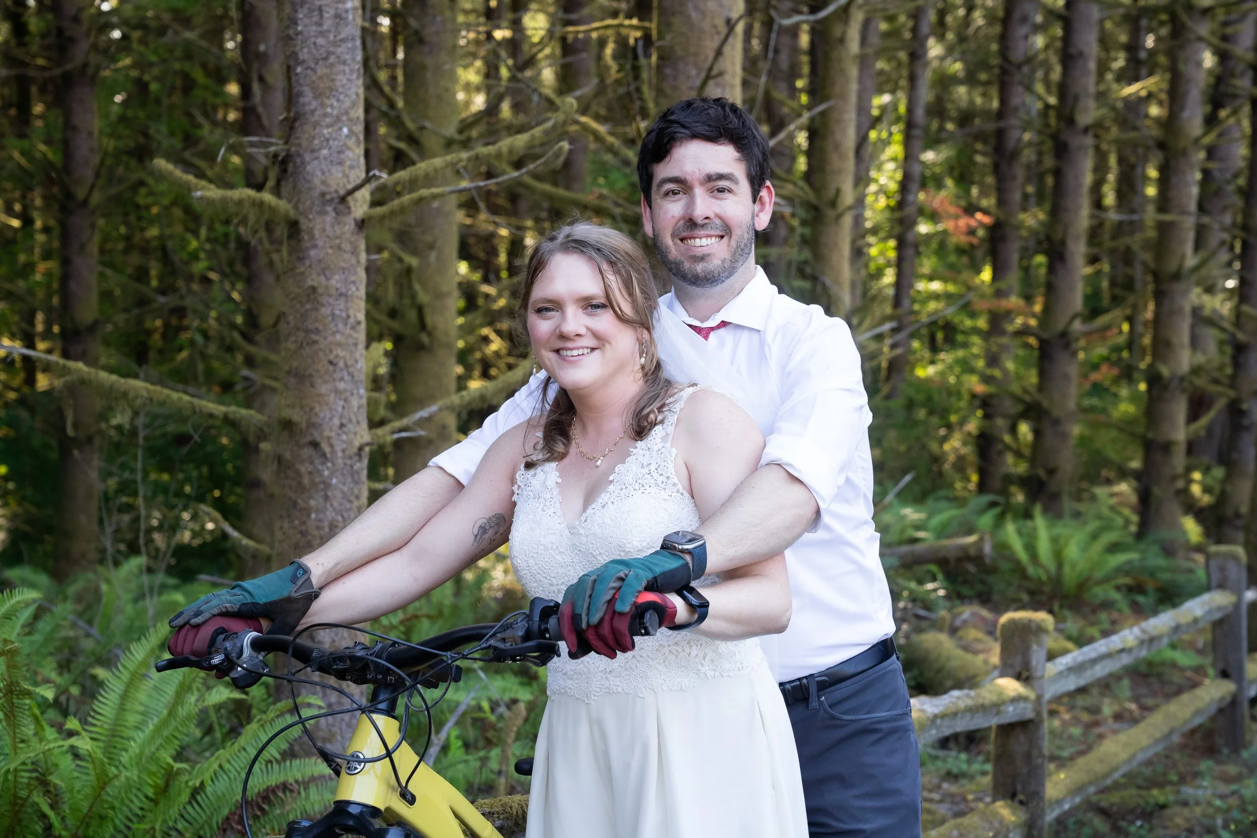 A couple standing together over a bright yellow bike during their mountain biking elopement on Galbraith Mountain in Bellingham, Washington