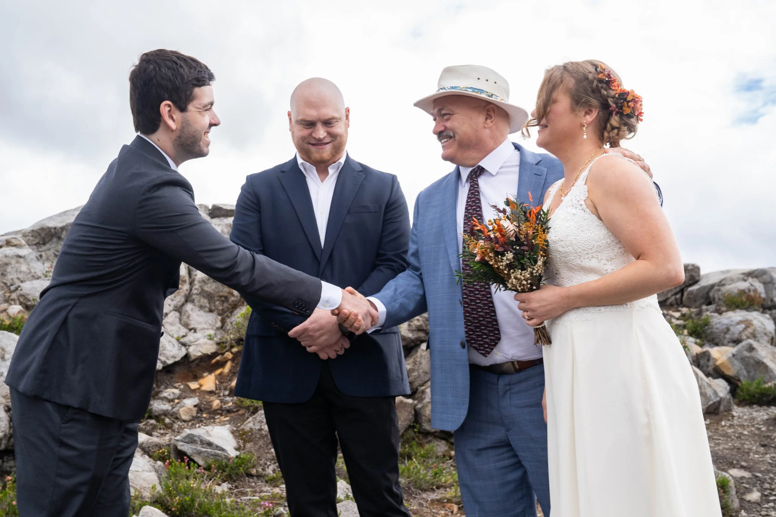 A groom shakes hands with his bride's father during an accessible micro wedding ceremony at Artist Point, while the bride and grooms' families look on.