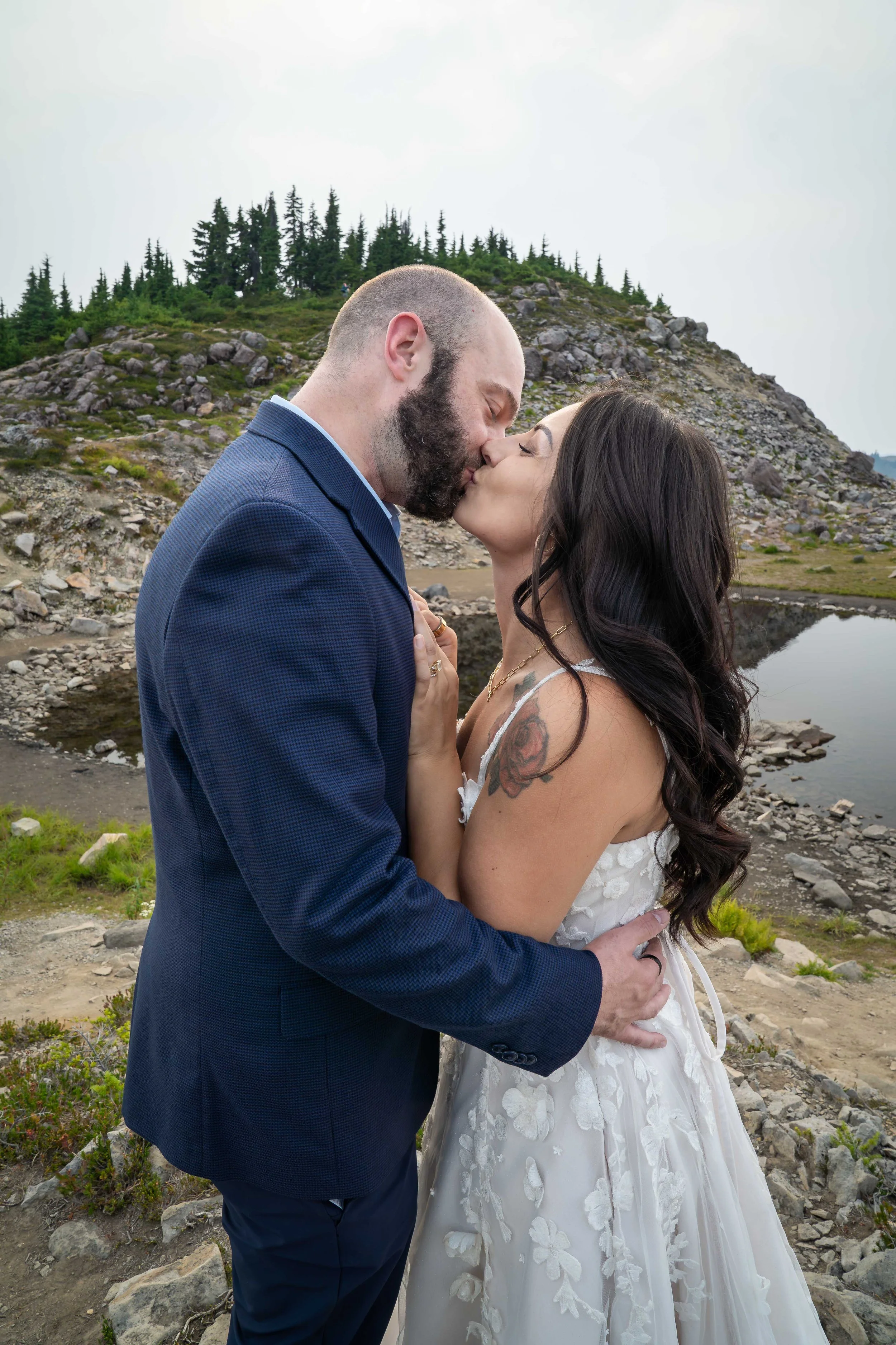 A bride and groom share their first kiss during their Artist Point elopement. They are standing close together in a rocky alpine meadow with a tarn visible behind them.