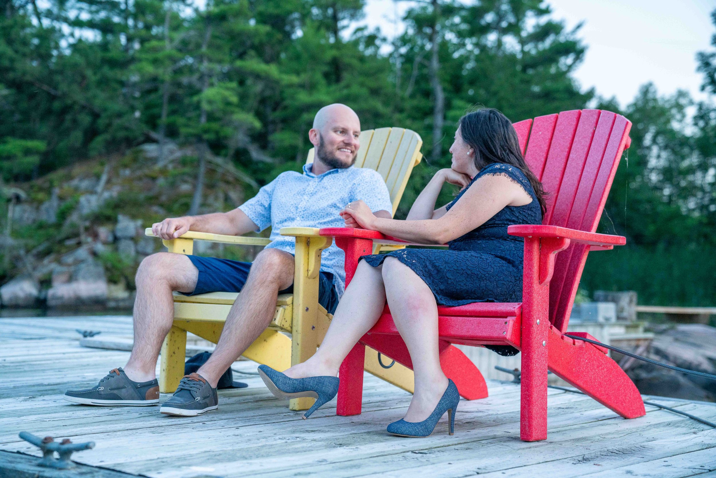 A couple in formal wear sitting on yellow and red Adirondack chairs on a dock in the San Juan Islands in Washington.