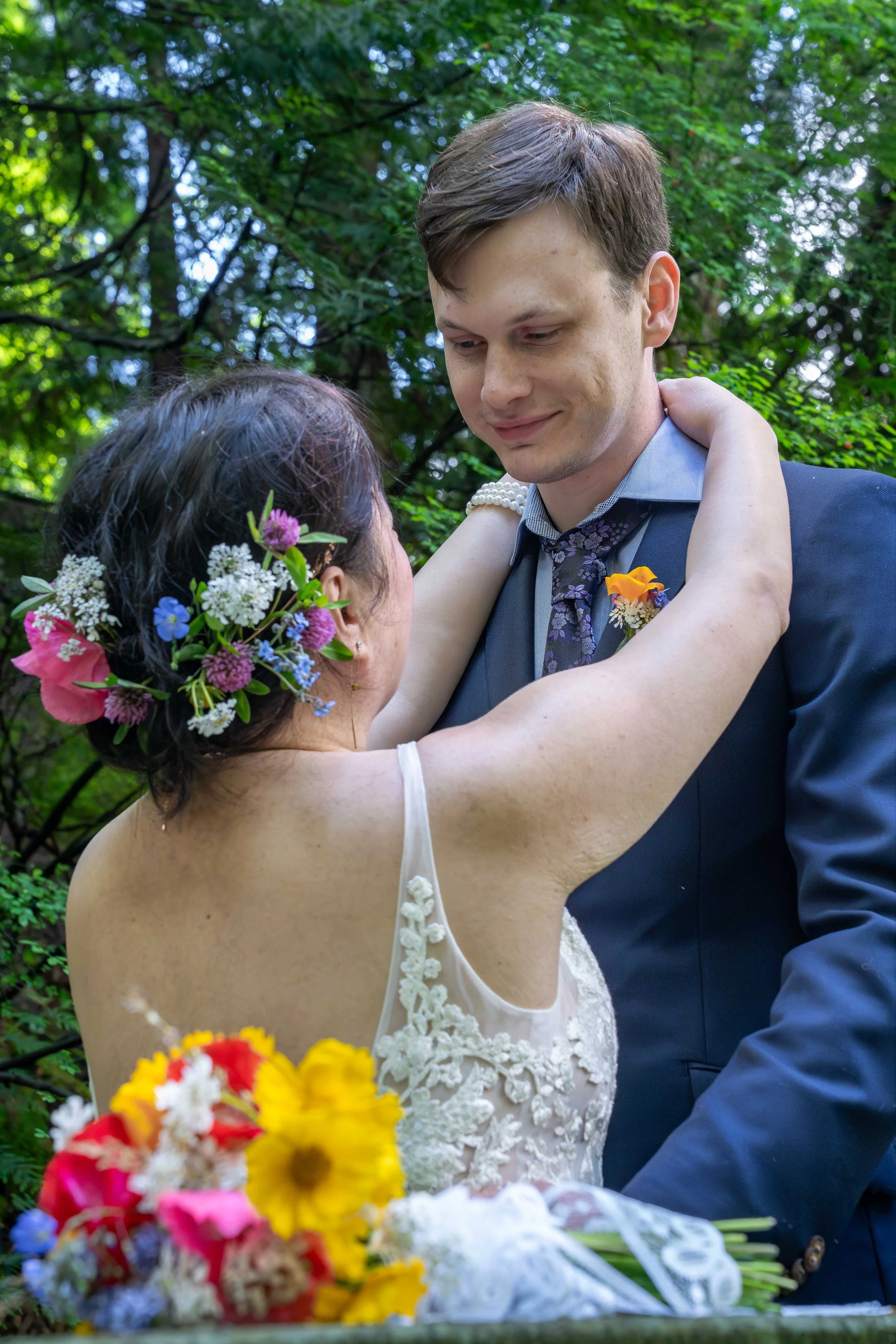 A bride wraps her arms around her groom's neck as he looks down at her after their first look ceremony during a Larrabee State Park elopement. The bride's bouquet is out of focus in the foreground.