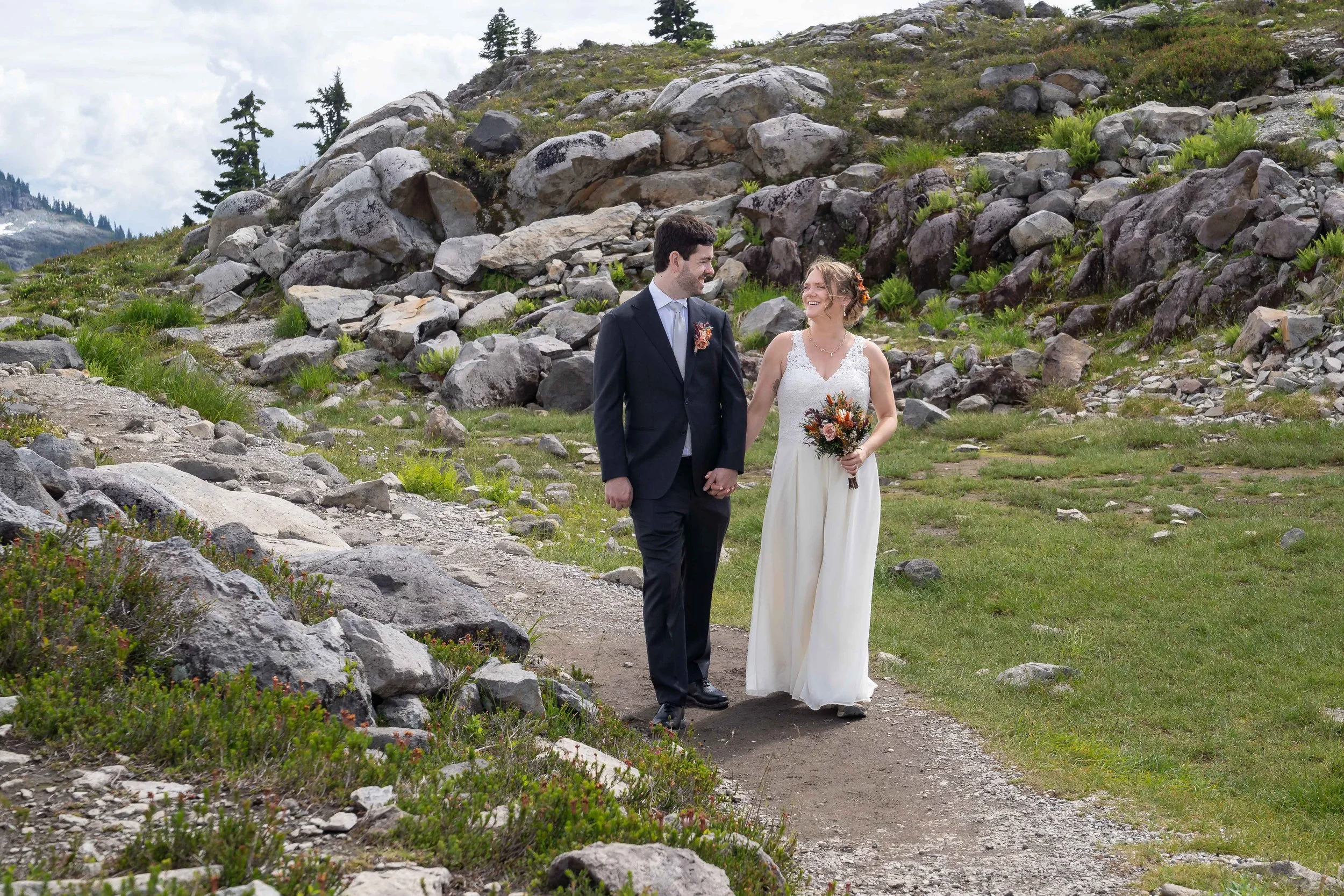 A photo of a bride and groom walking on a trail at Artist Point after eloping. The couple is holding hands and laughing as they walk towards the camera.