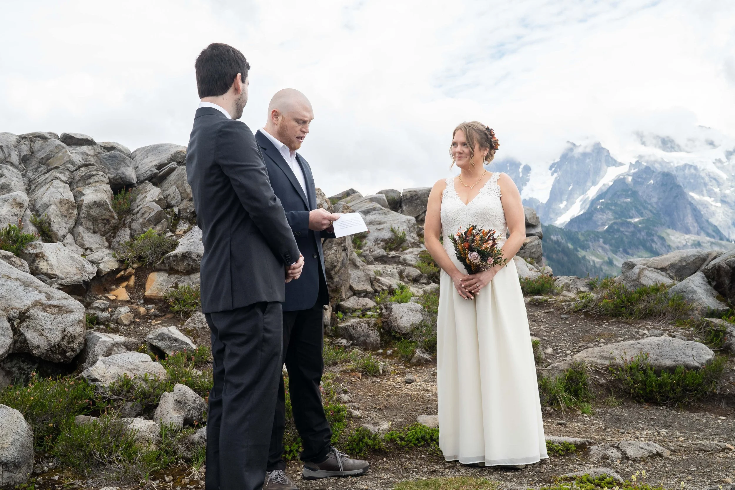 Photo of a bride, groom, and their officiant during an elopement ceremony at Artist Point, with Mt. Shuksan visible behind them in a cloud.