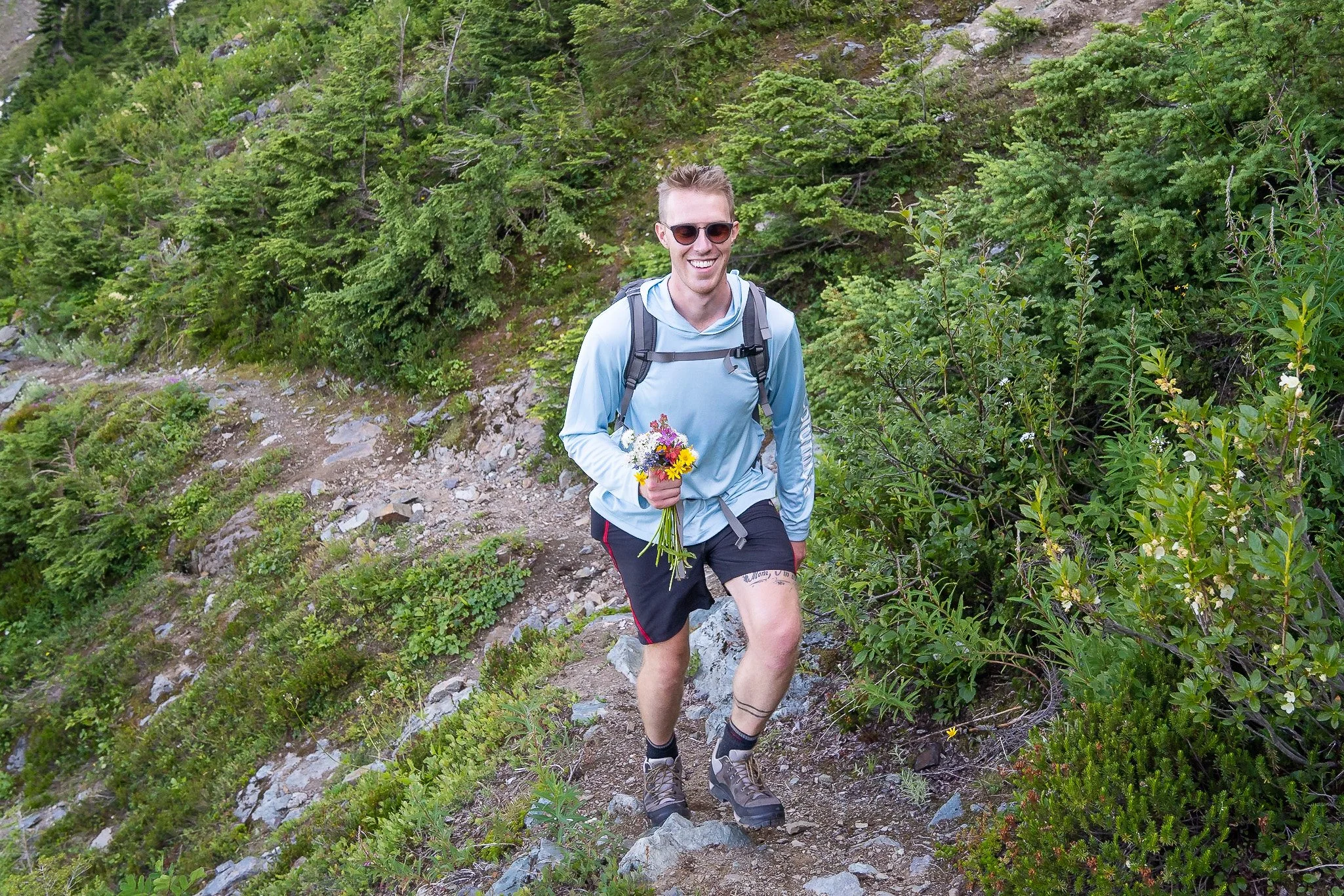 A photo of the groom in a backcountry elopement hiking up the trail while holding a bouquet of freshly picked wildflowers.