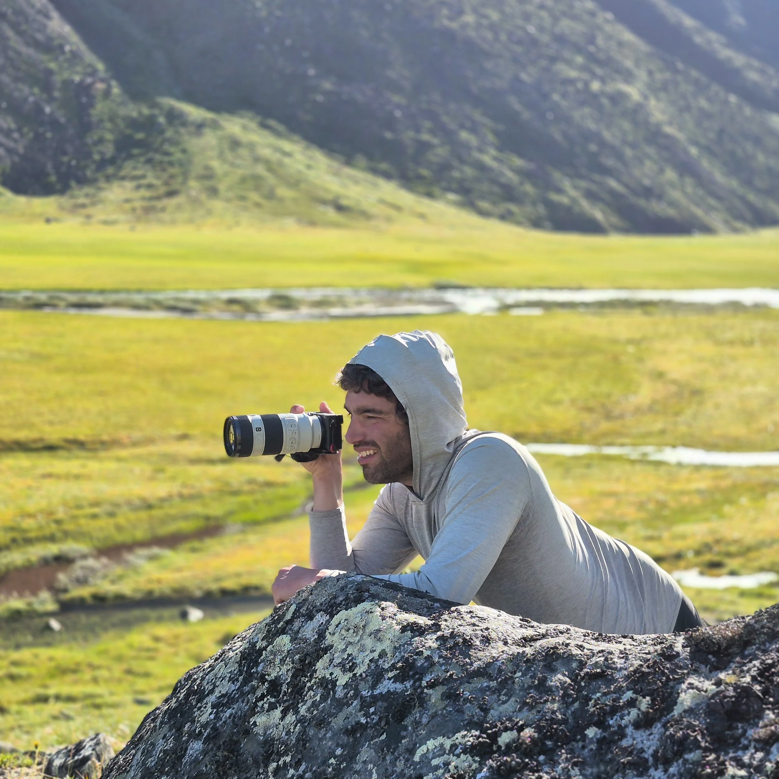 A photo of Michael Graw, the elopement photographer behind Wandering Sole Studios. He's holding a camera with a telephoto lens while leaning on a rock in the middle of a large, open valley.