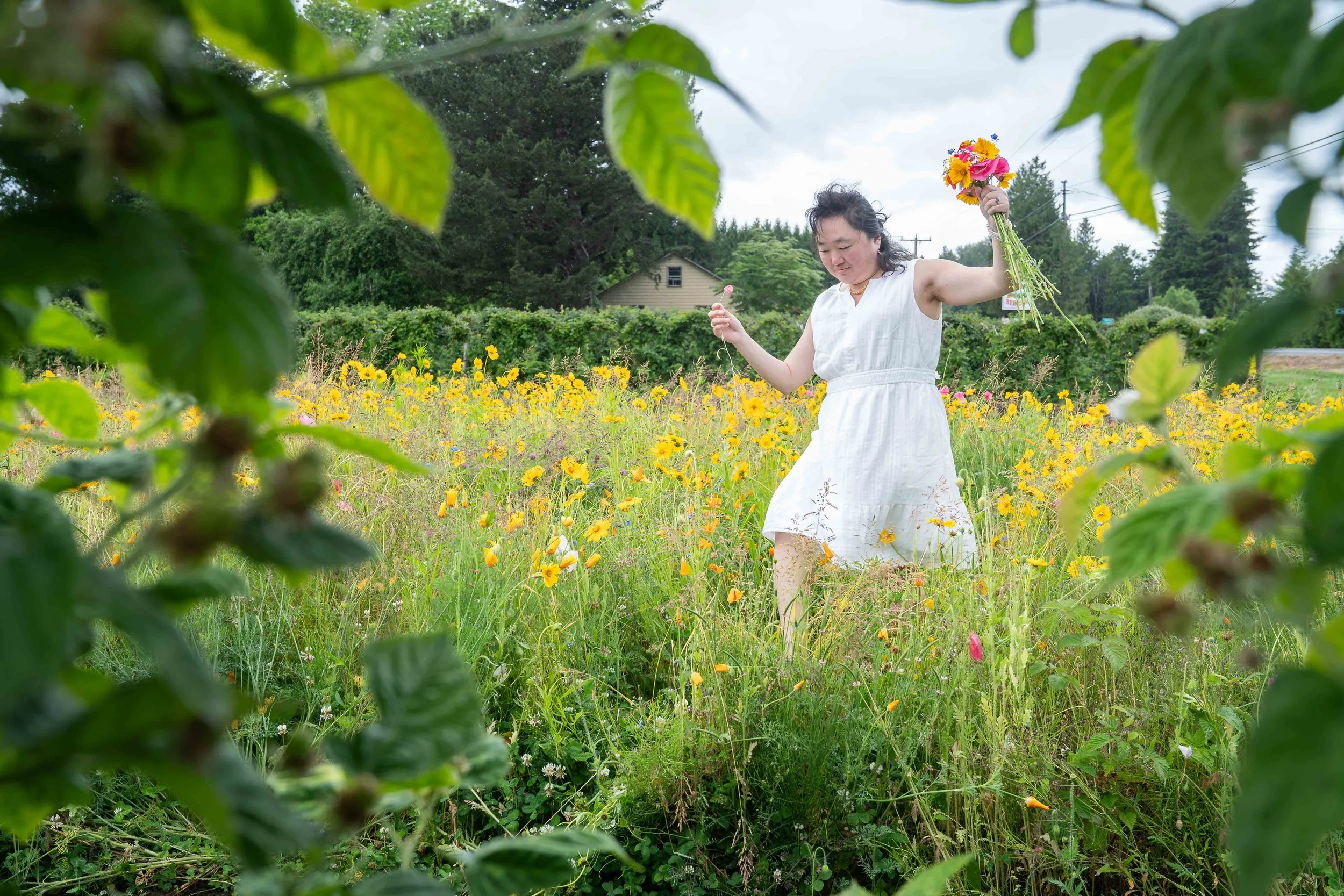 A photo of a bride in a white dress walking through a field of flowers, holding a bouquet in her hands, during a Bellingham elopement.