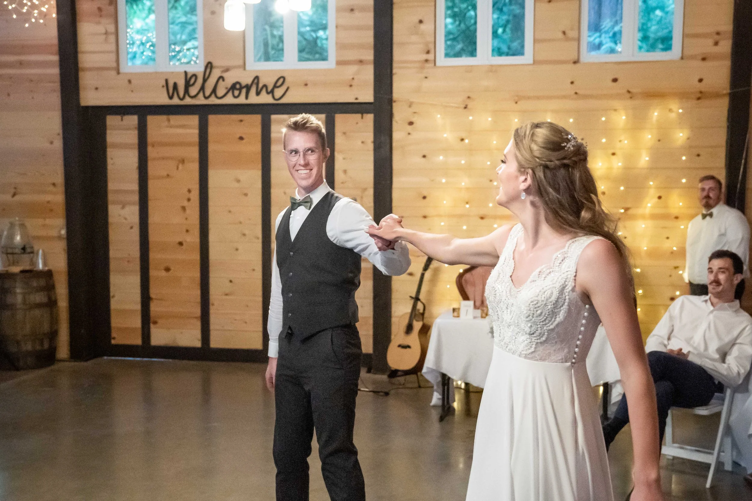 A bride and groom's first dance at their wedding at Creekside Celebrations in Sedro-Woolley, Washington. The bride and groom are holding hands with their arms extended while their wedding guests look on.