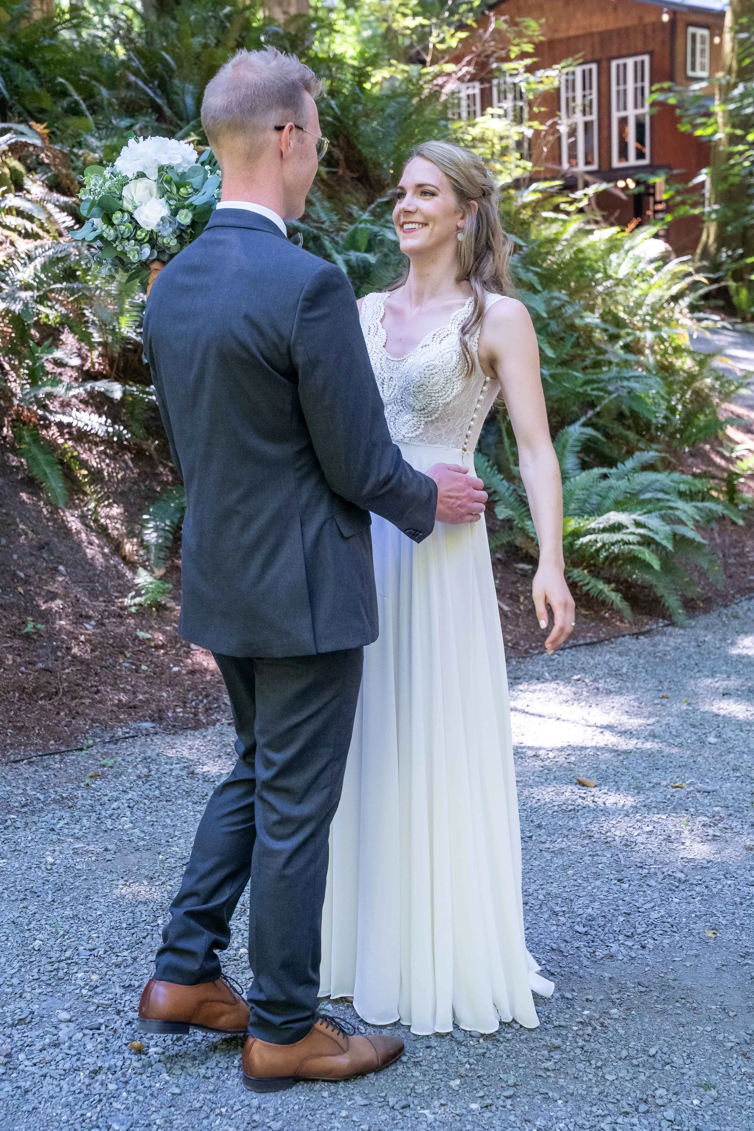 A groom in a suit seeing his bride in a wedding dress for the first time during a first look at a Skagit County, Washington wedding. The bride is smiling and holding a bouquet of white flowers.