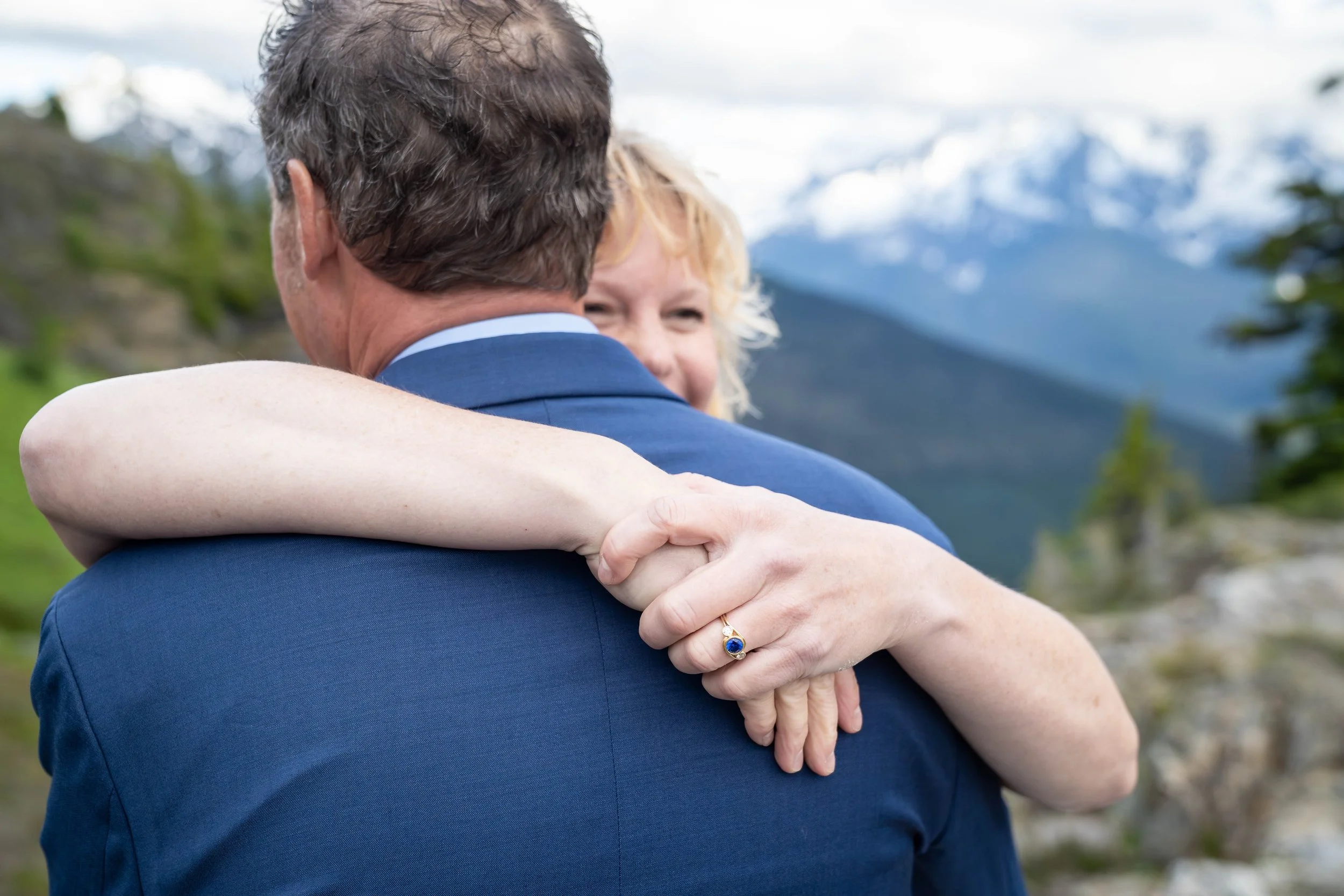 A bride has her arms wrapped over the shoulders of her groom so that her ring is clearly visible during a North Cascades elopement ceremony at Yellow Aster Butte. Mt. Shuksan is visible behind them.