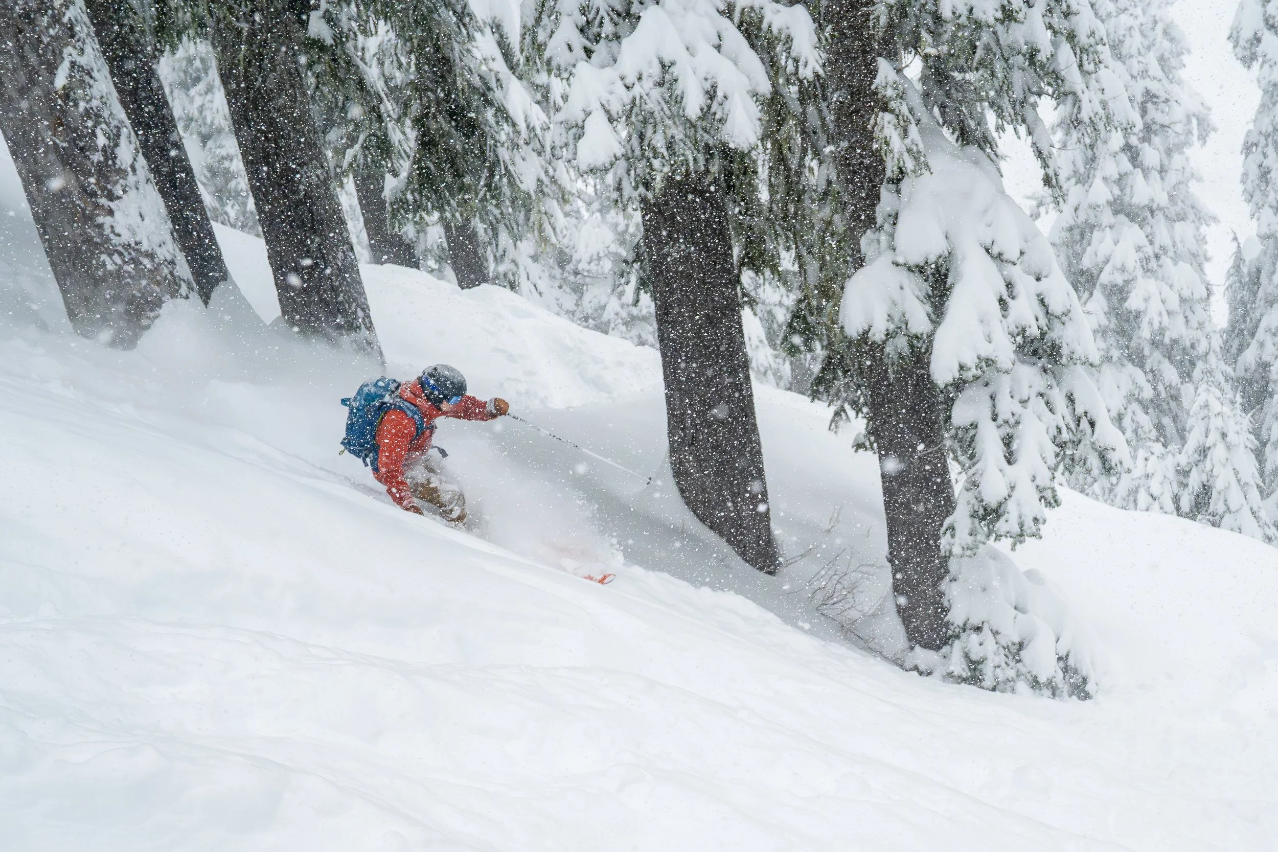 Photo of a man in a red jacket backcountry skiing through deep powder above Source Lake, near Snoqualmie Pass, Washington.