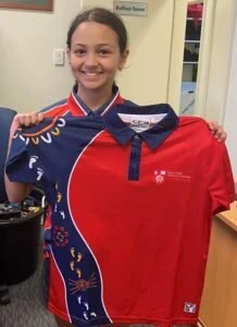 Young girl smiling and holding a red and blue sports jersey in an indoor setting.