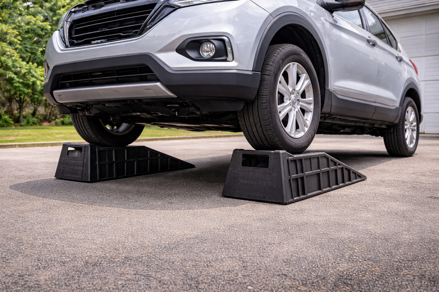 A silver SUV is lifted off the ground using black wheel chocks placed behind the front tires.