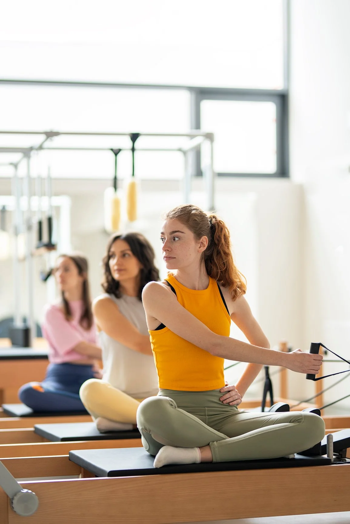 Three women practicing Pilates on reformer machines in a bright fitness studio.