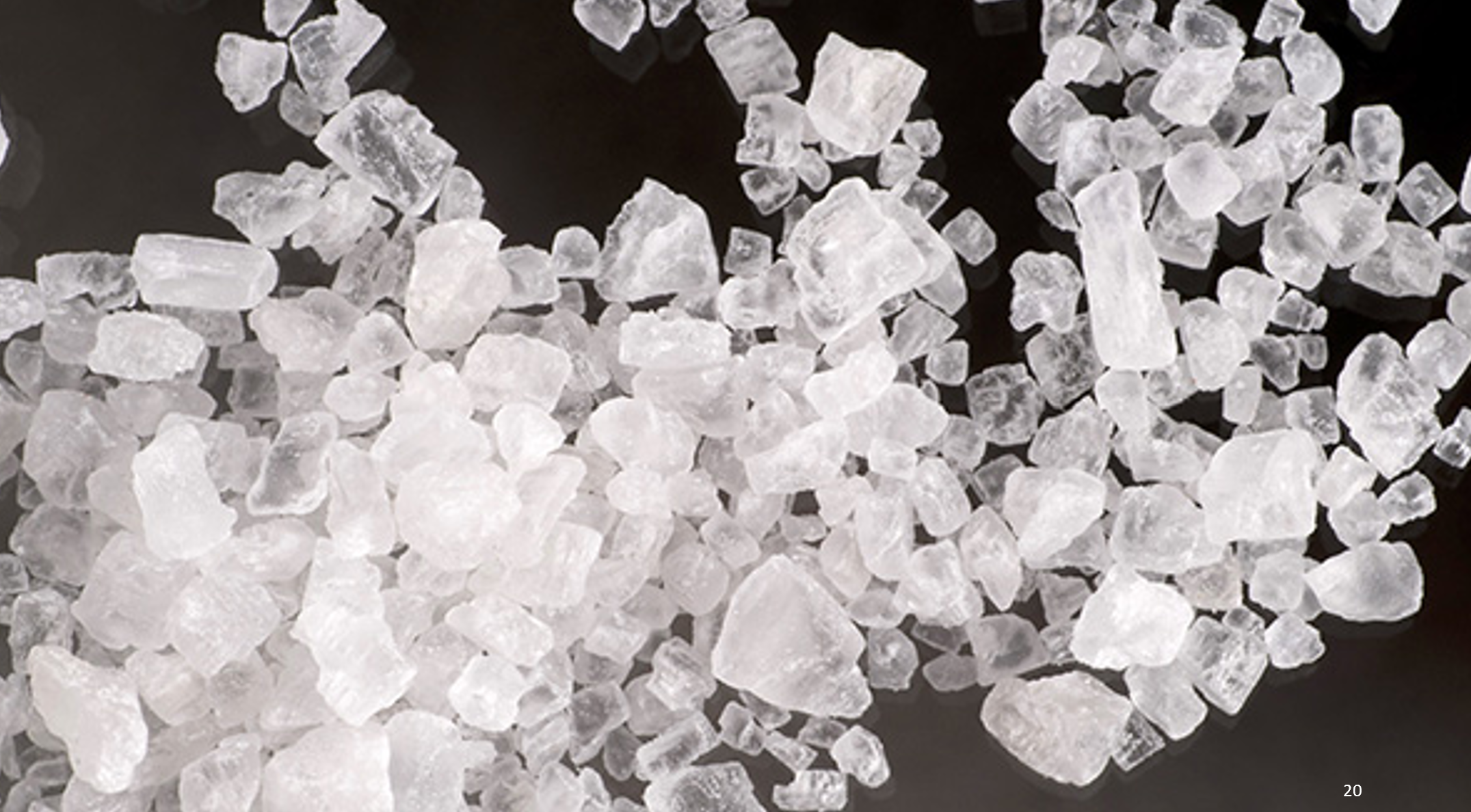 Close-up of white rock salt crystals scattered on a black surface.
